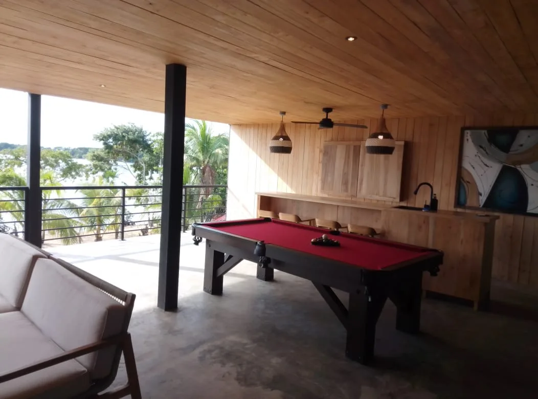 Sala de juegos con una mesa de billar de paño rojo junto a un balcón abierto.