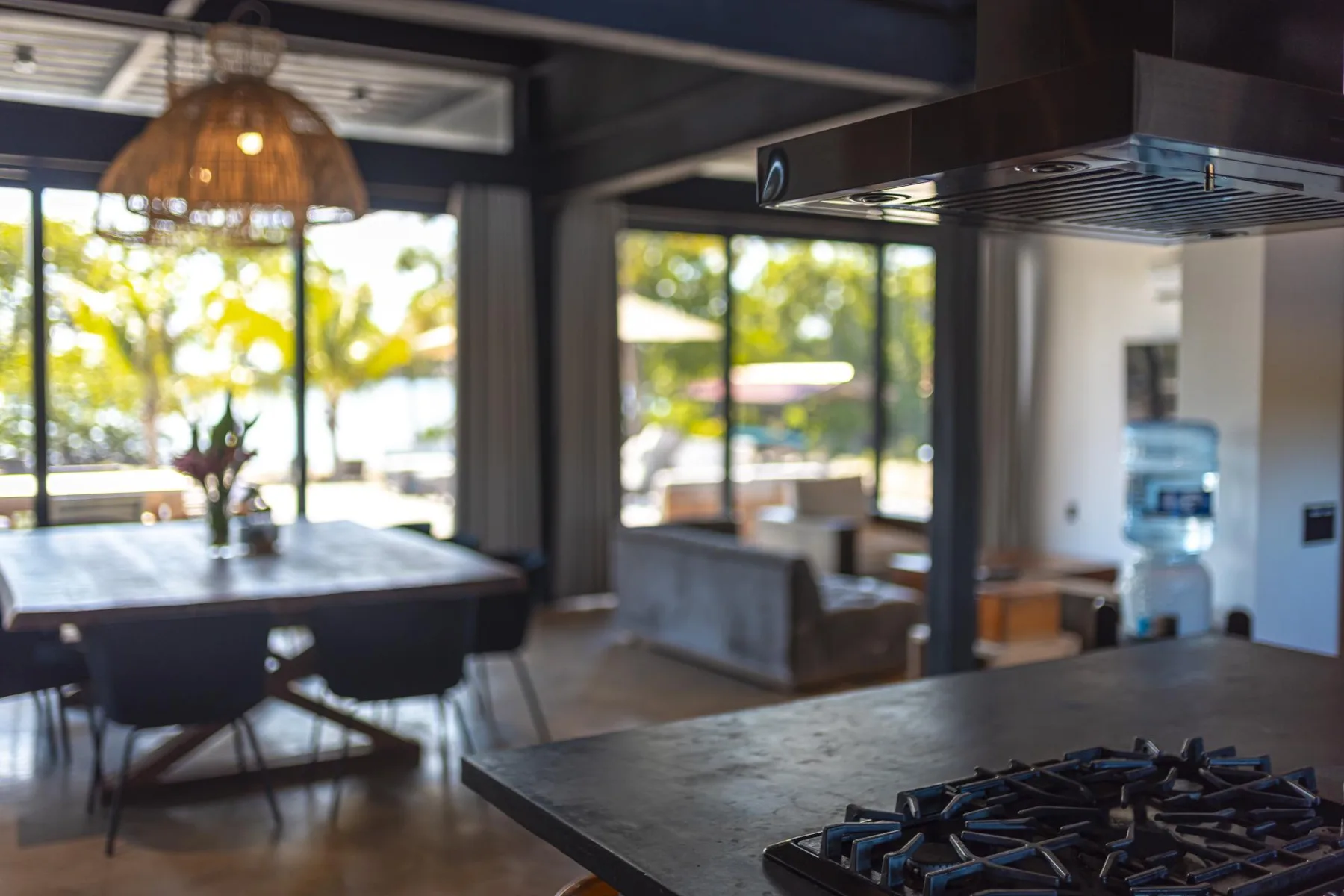 Un comedor con una mesa junto a grandes ventanas y una placa de cocina en primer plano.