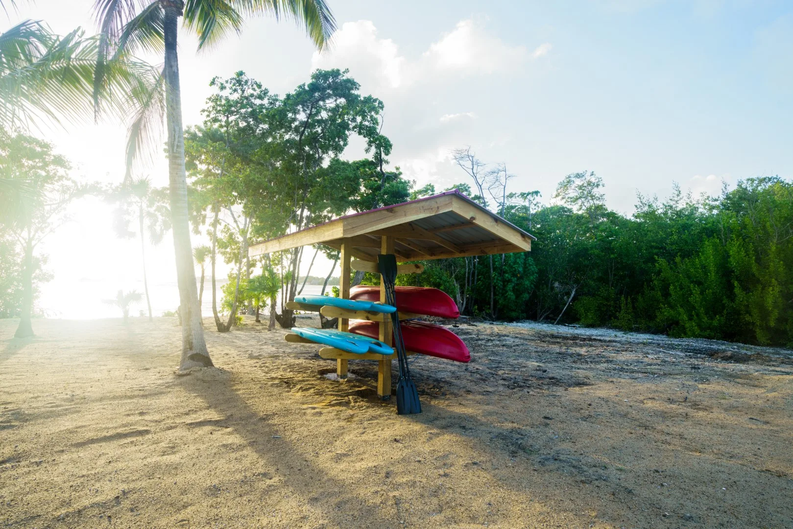 Una zona exterior arenosa con kayaks de colores guardados bajo un pequeño refugio.