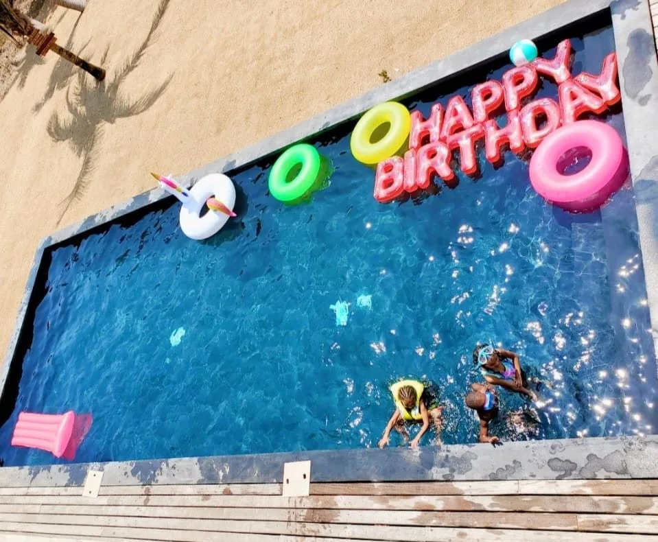 Una piscina al aire libre tiene adornos coloridos de cumpleaños y personas nadando.