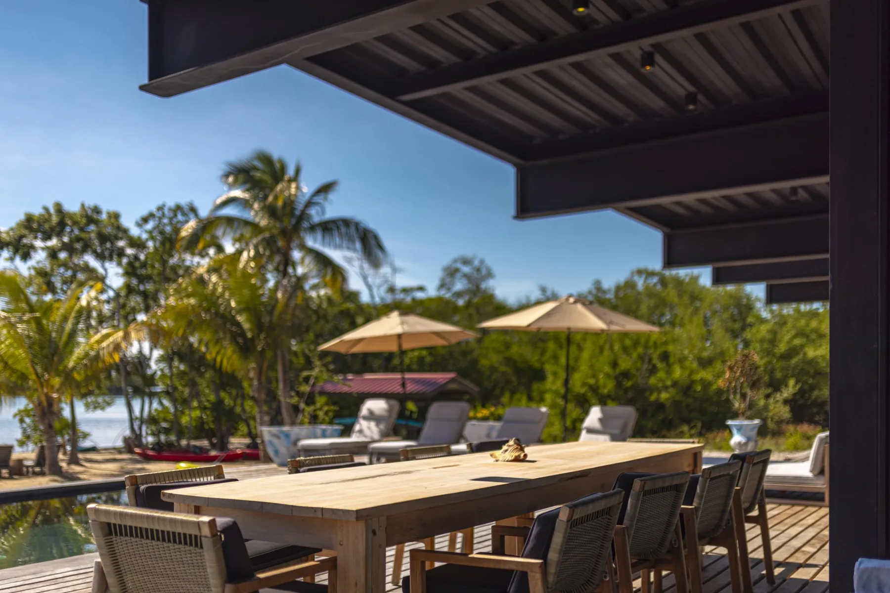 Un comedor al aire libre con una mesa larga, asientos y sombrillas.