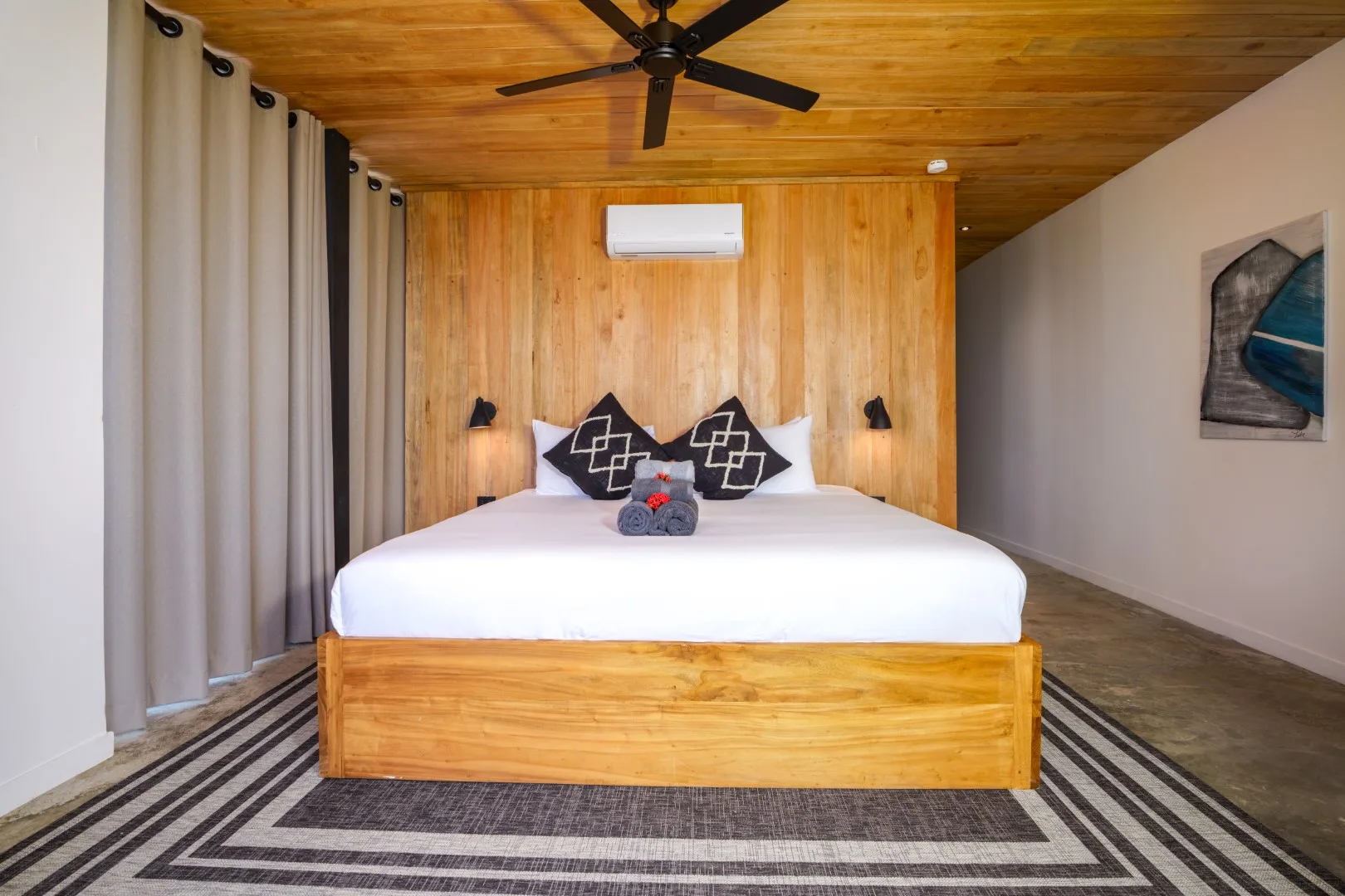 Un dormitorio con cama de madera, alfombra estampada y techo revestido de madera.