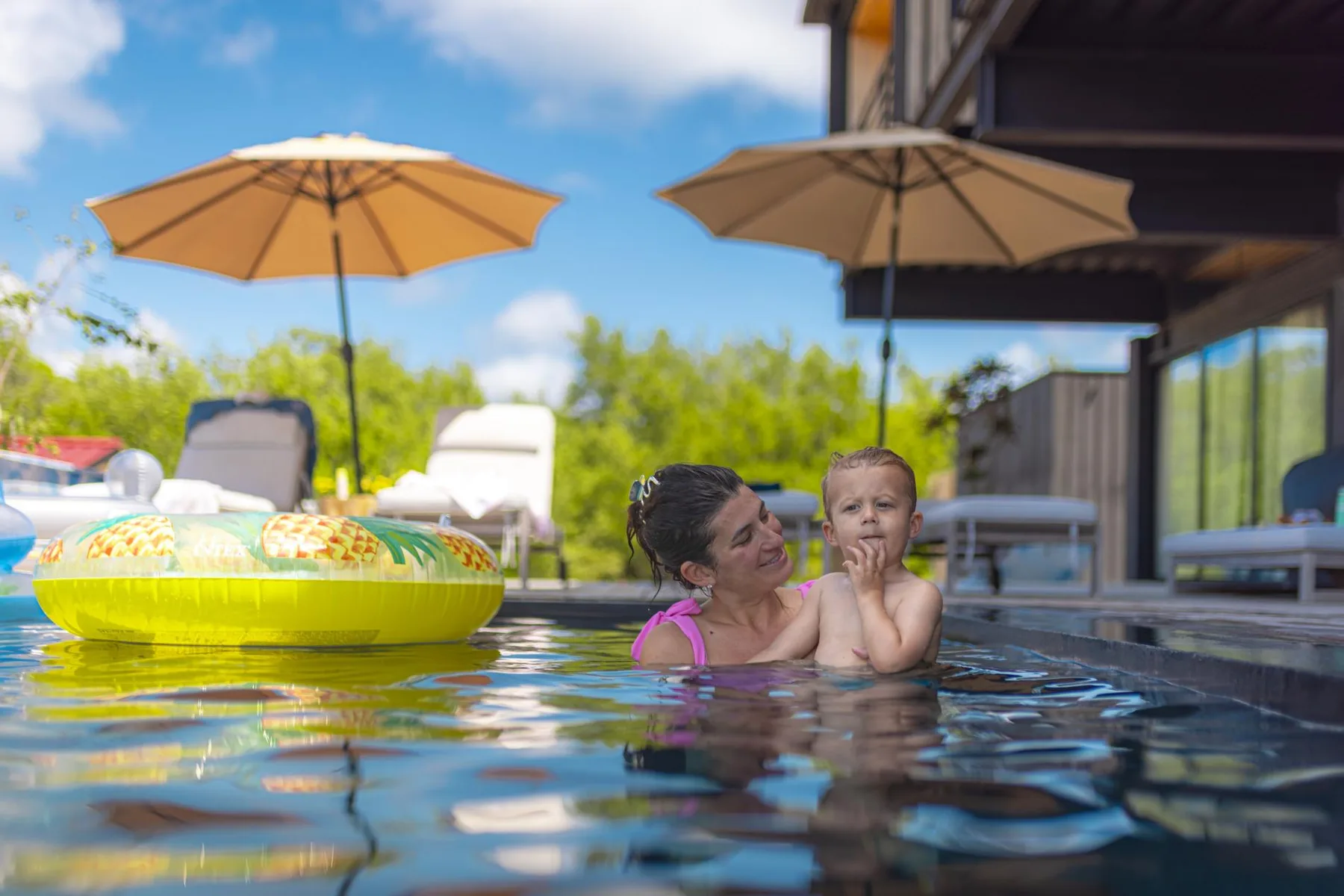Una mujer y un niño disfrutan de un baño en una piscina exterior bajo sombrillas.