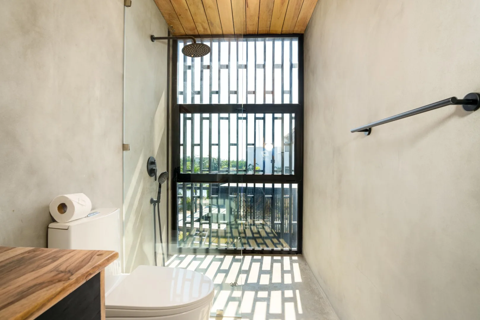 Un baño con ducha, inodoro y una ventana alta por la que entra luz natural.