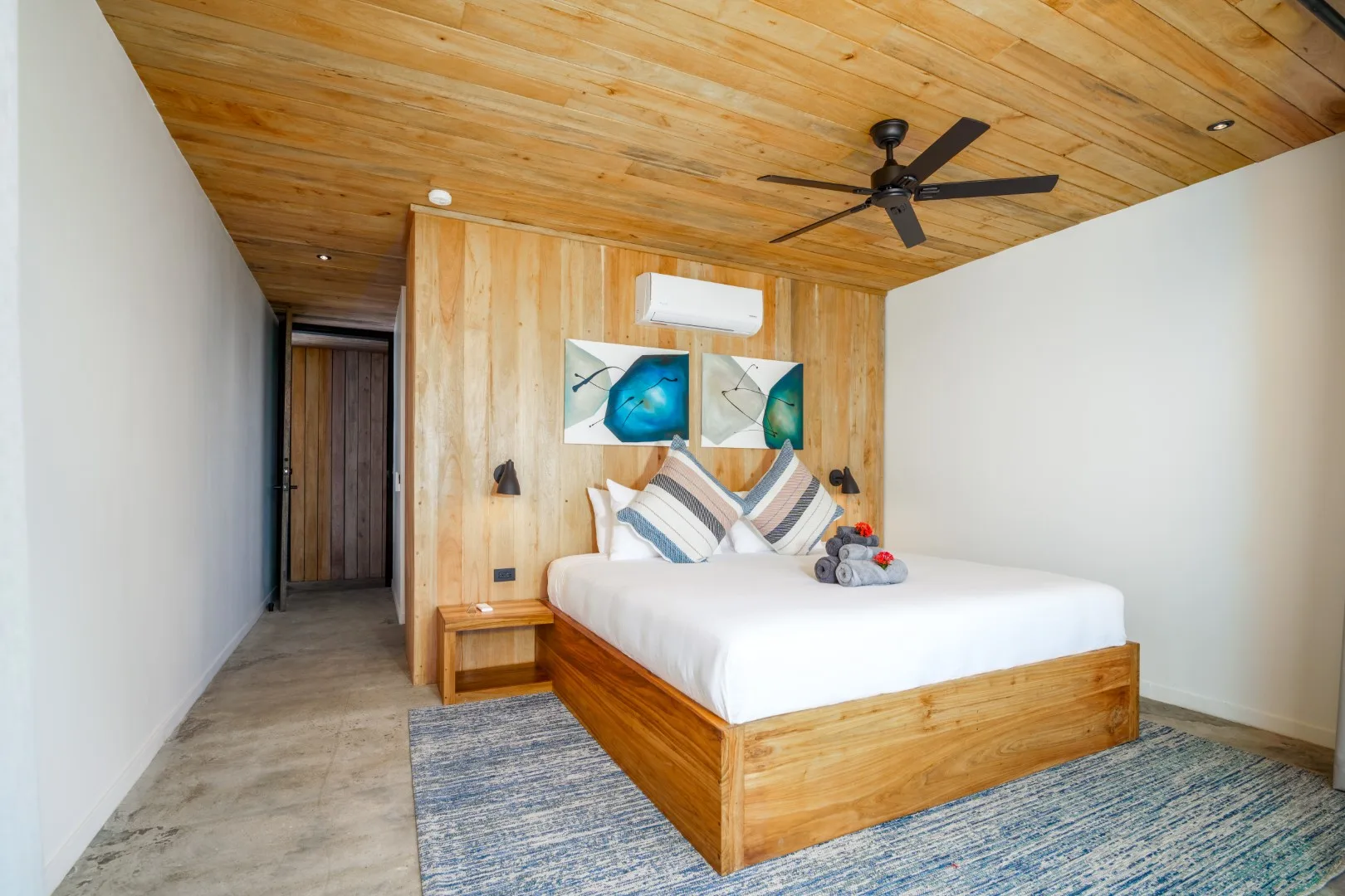 Un dormitorio con una cama de madera, arte colorido y un ventilador de techo.