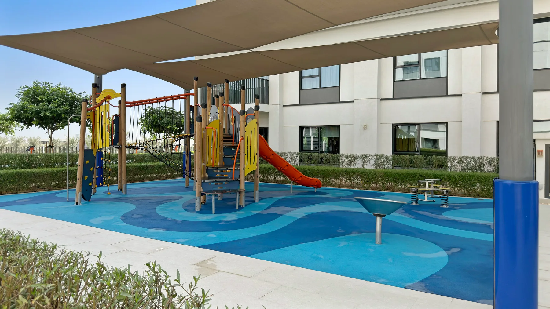 Zona común: Un parque infantil al aire libre, con sombra, juegos para trepar y un tobogán.