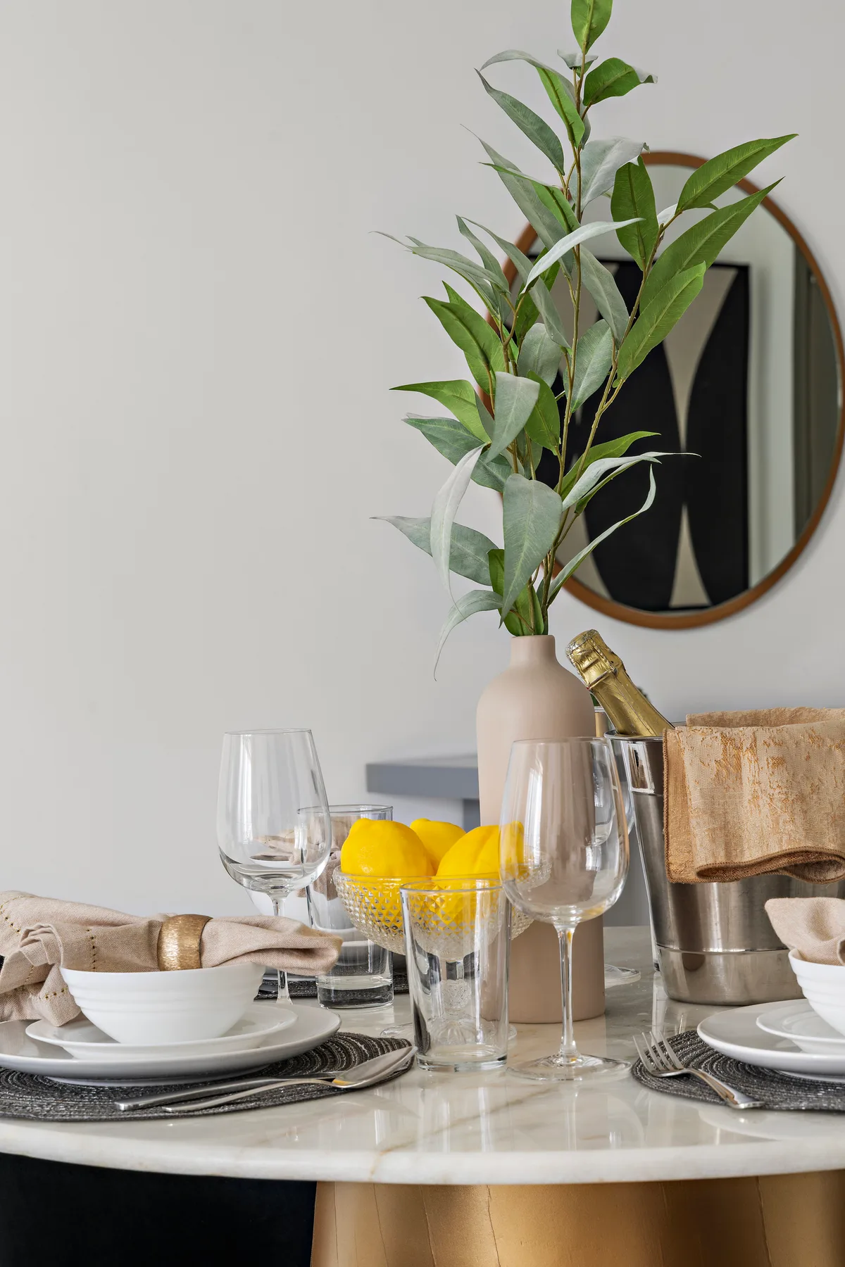 Una mesa de comedor está puesta con cristalería, un jarrón con ramas verdes y limones.