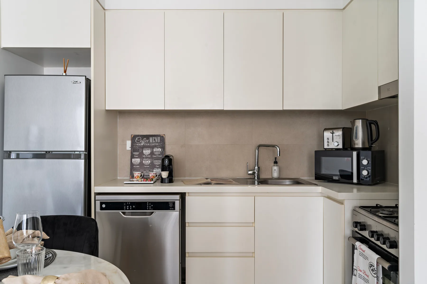 Una cocina compacta con gabinetes blancos, un refrigerador y electrodomésticos de acero inoxidable.