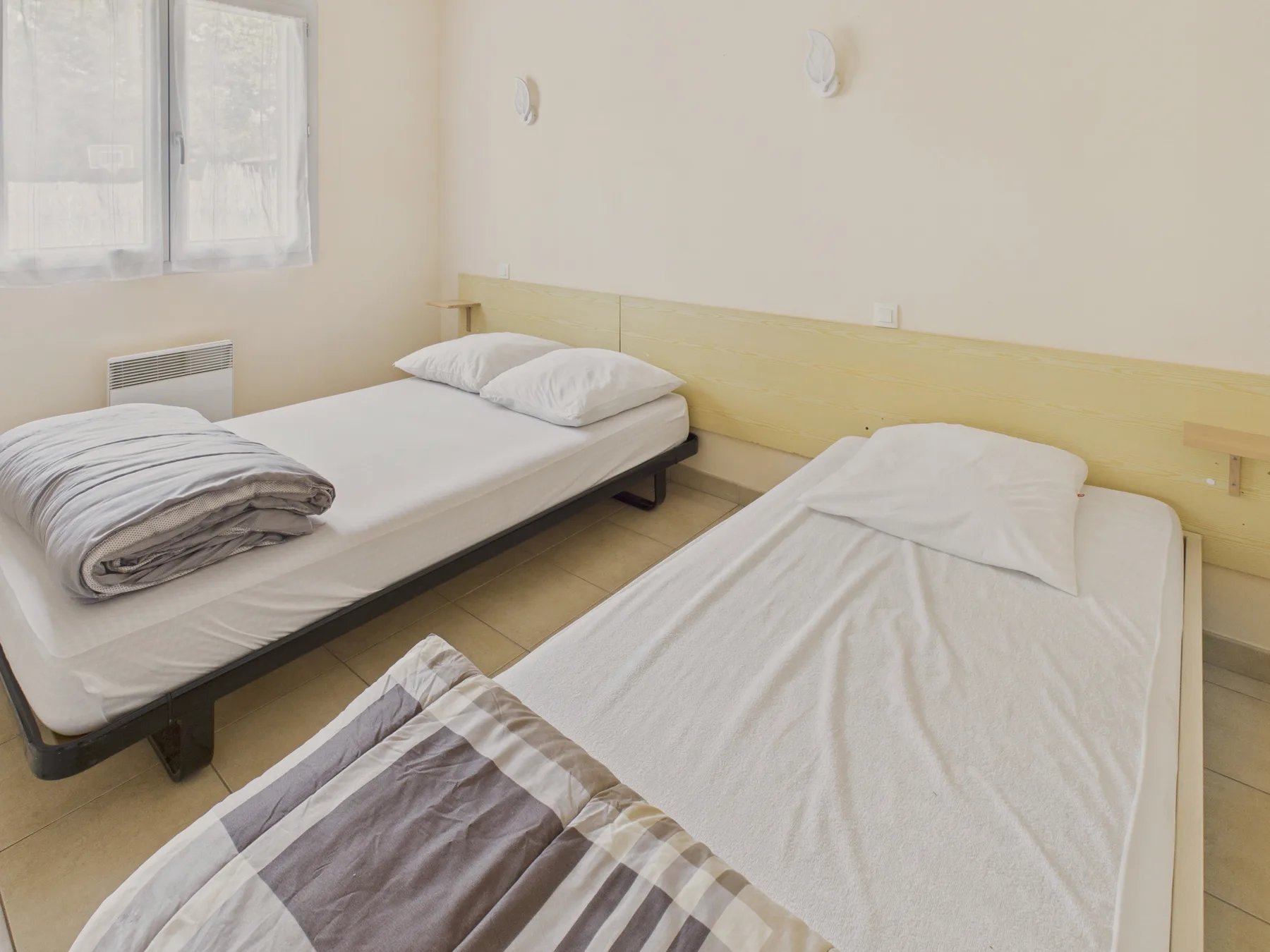A bedroom with two single beds, white bedding, and a window.