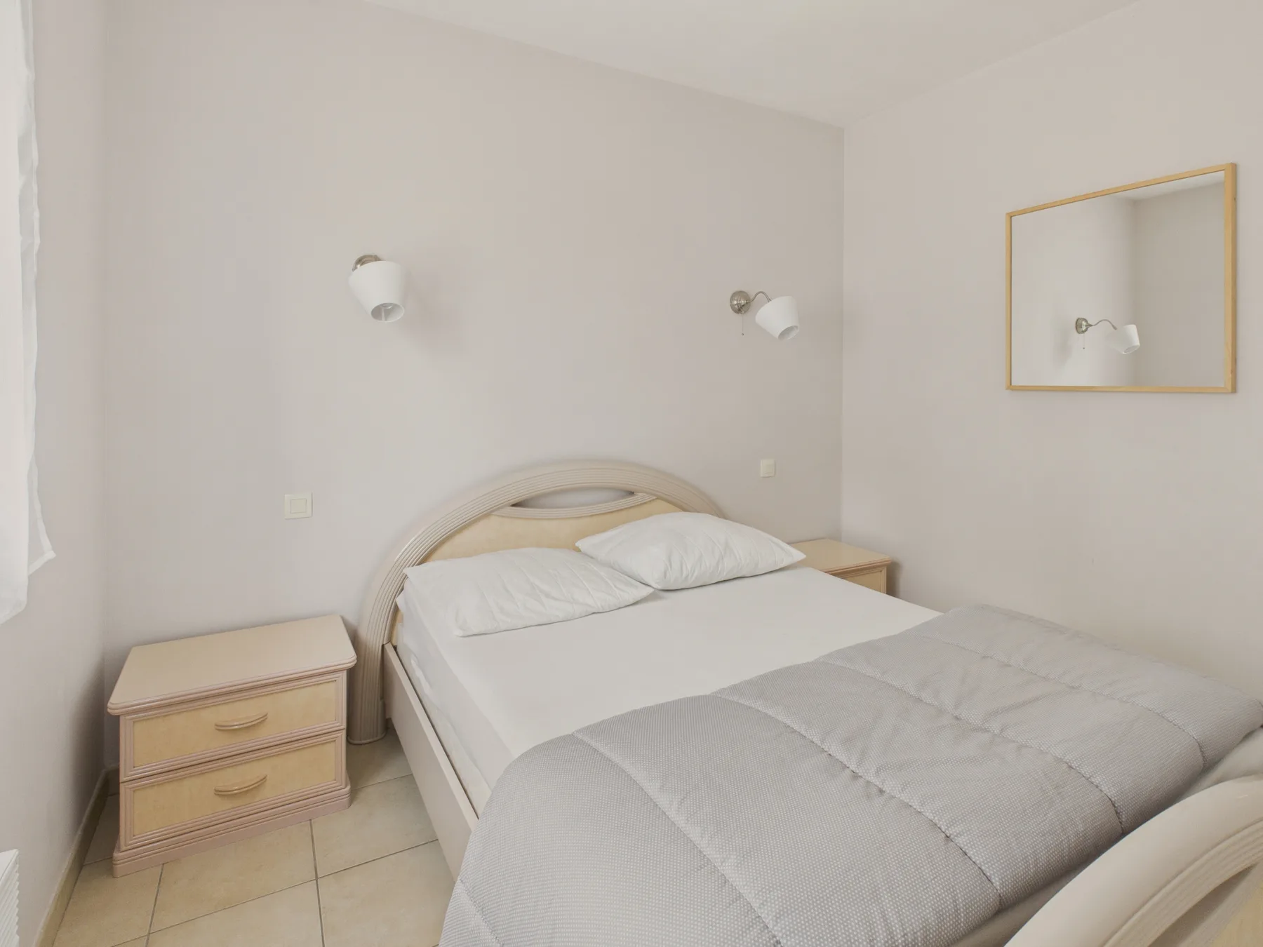 A bedroom with a double bed, bedside table, and wall lights.