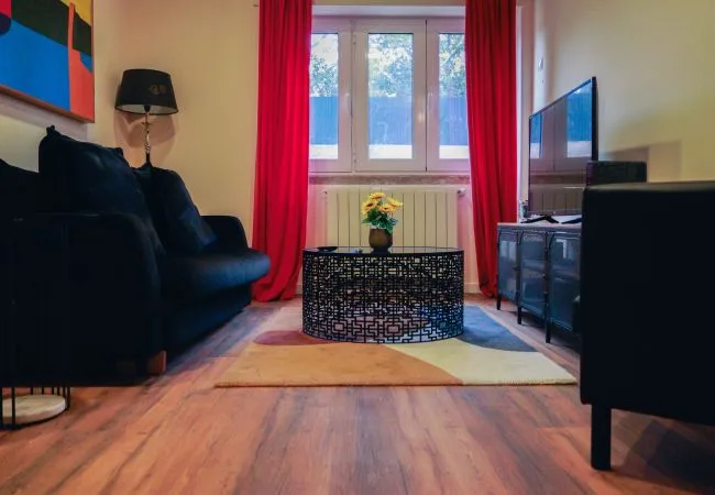 Una sala de estar con asientos oscuros, una mesa de centro estampada y cortinas rojas.