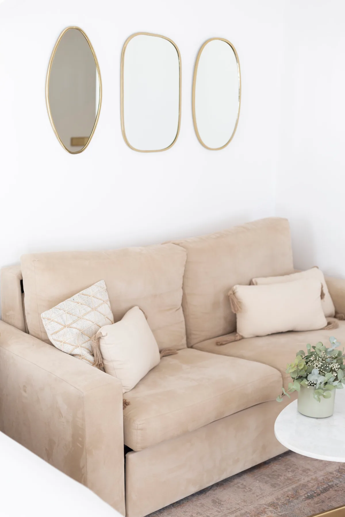 Espacio representativo del hotel: Un sofá beige con cojines decorativos está debajo de tres espejos ovalados.