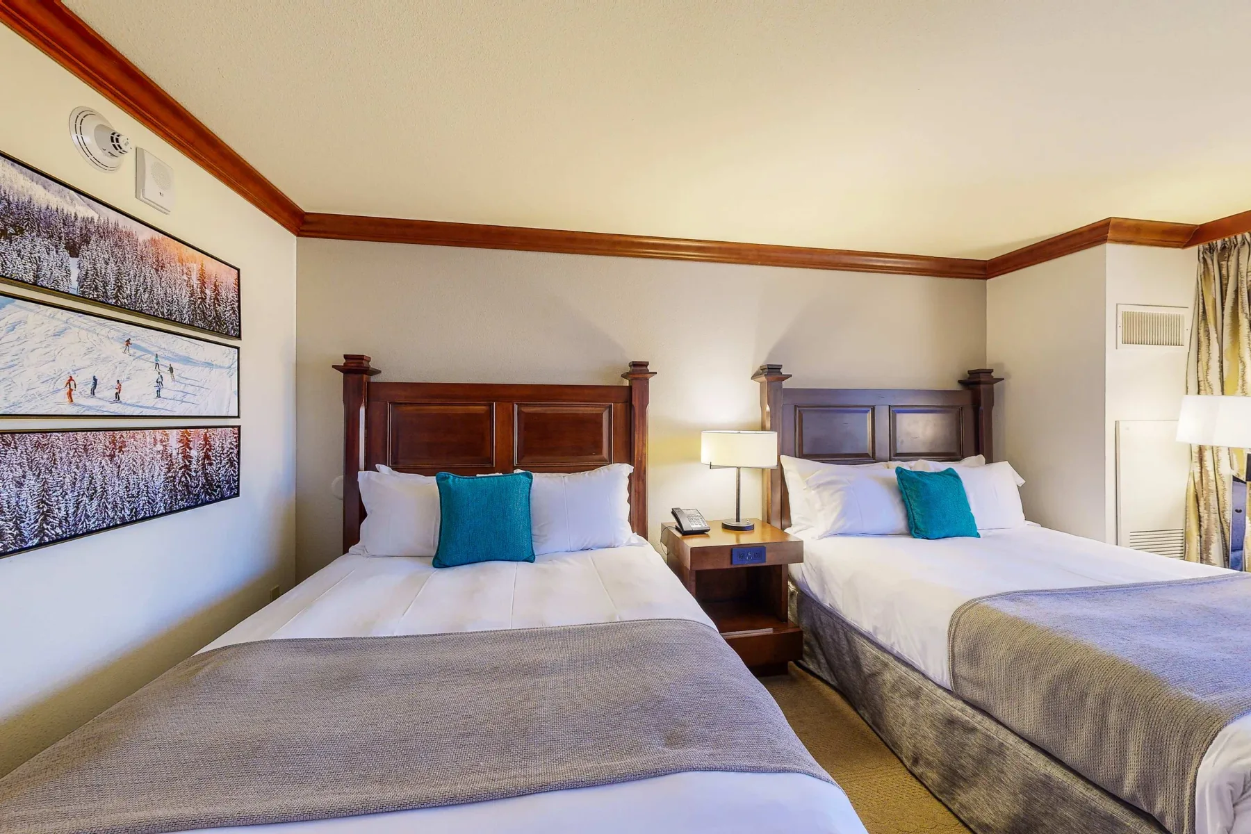 A bedroom with two beds, bedside tables, and framed artwork on the wall.