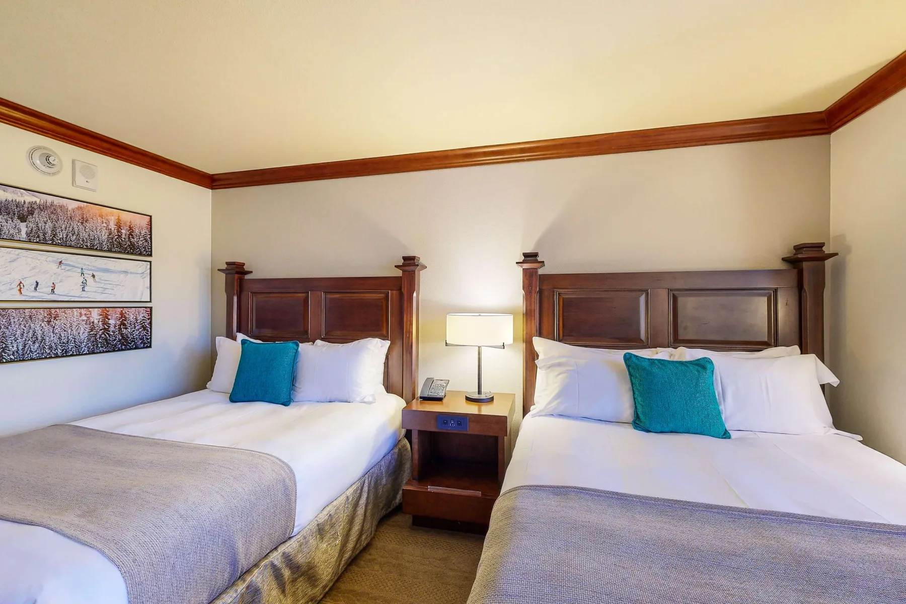 A bedroom with two beds, dark wooden headboards, and a bedside table.