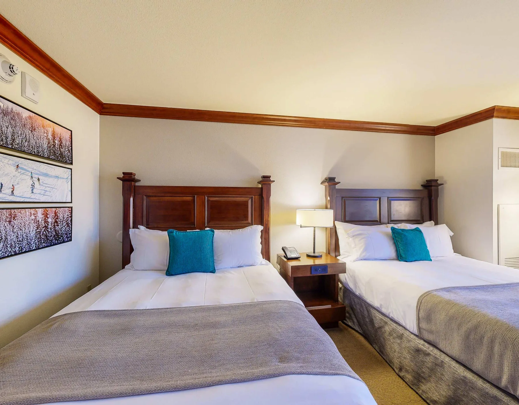 A bedroom with two beds and framed landscape prints on the wall.