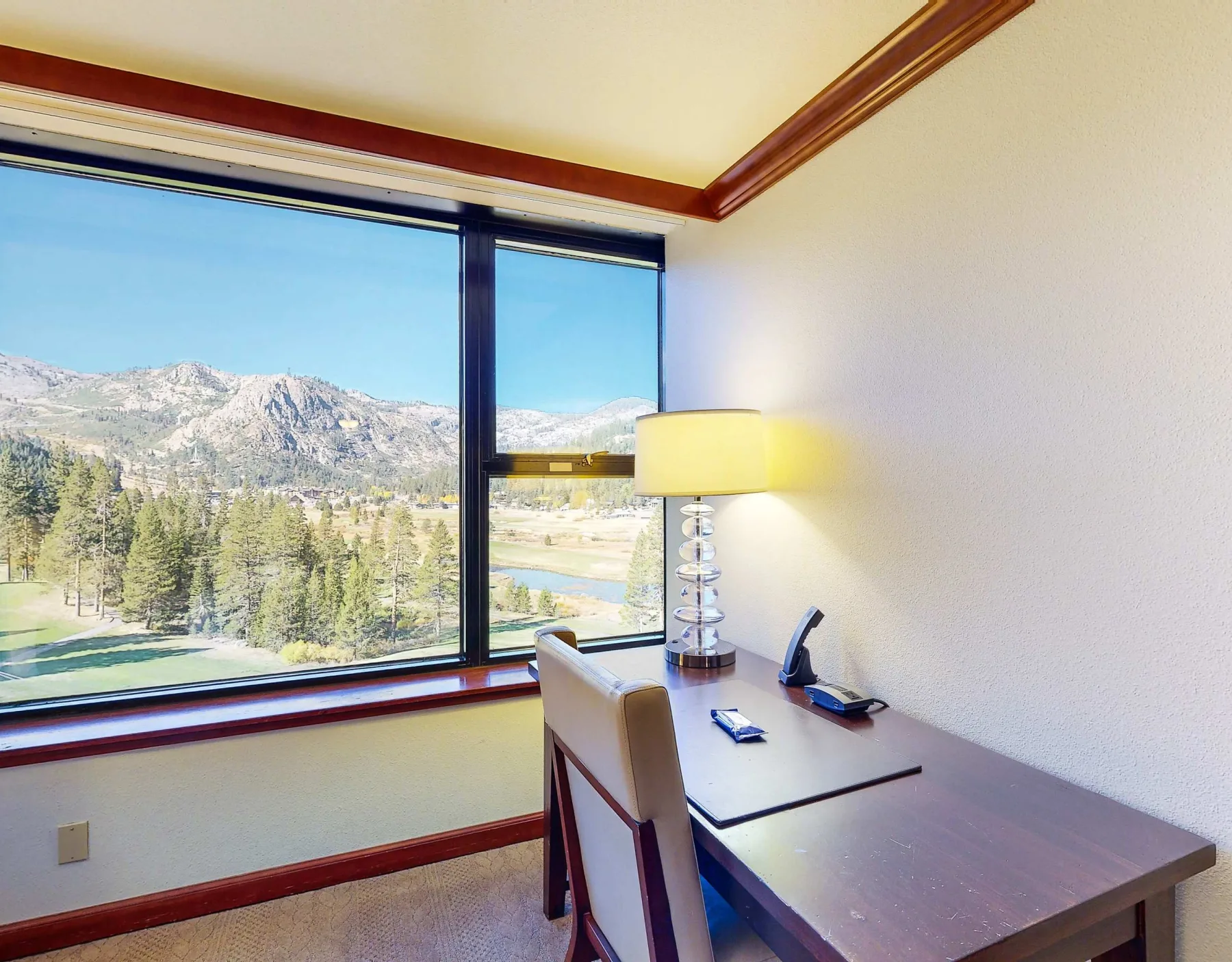 A desk and chair sit beside a large window overlooking trees and mountains.