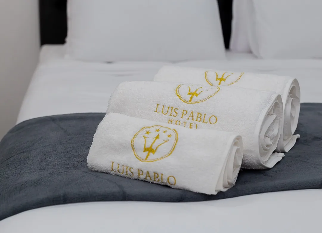 Espacio representativo del hotel: Toallas blancas dobladas están sobre una manta oscura en la cama.