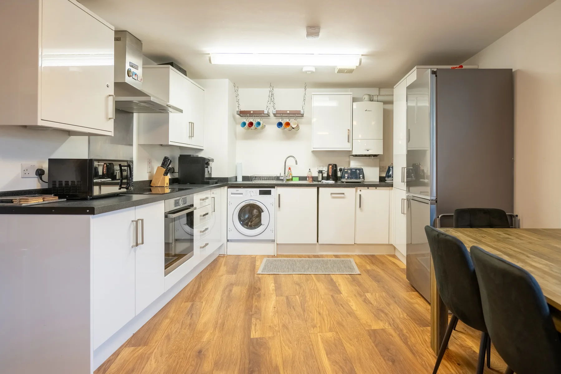 A bright kitchen with white cabinets, dark countertops, and a wooden dining table.