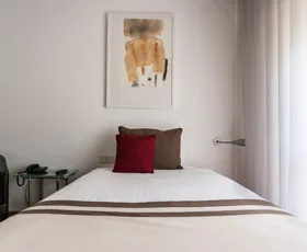 Espacio representativo del hotel: Un dormitorio con una cama bien tendida y una obra de arte encima.
