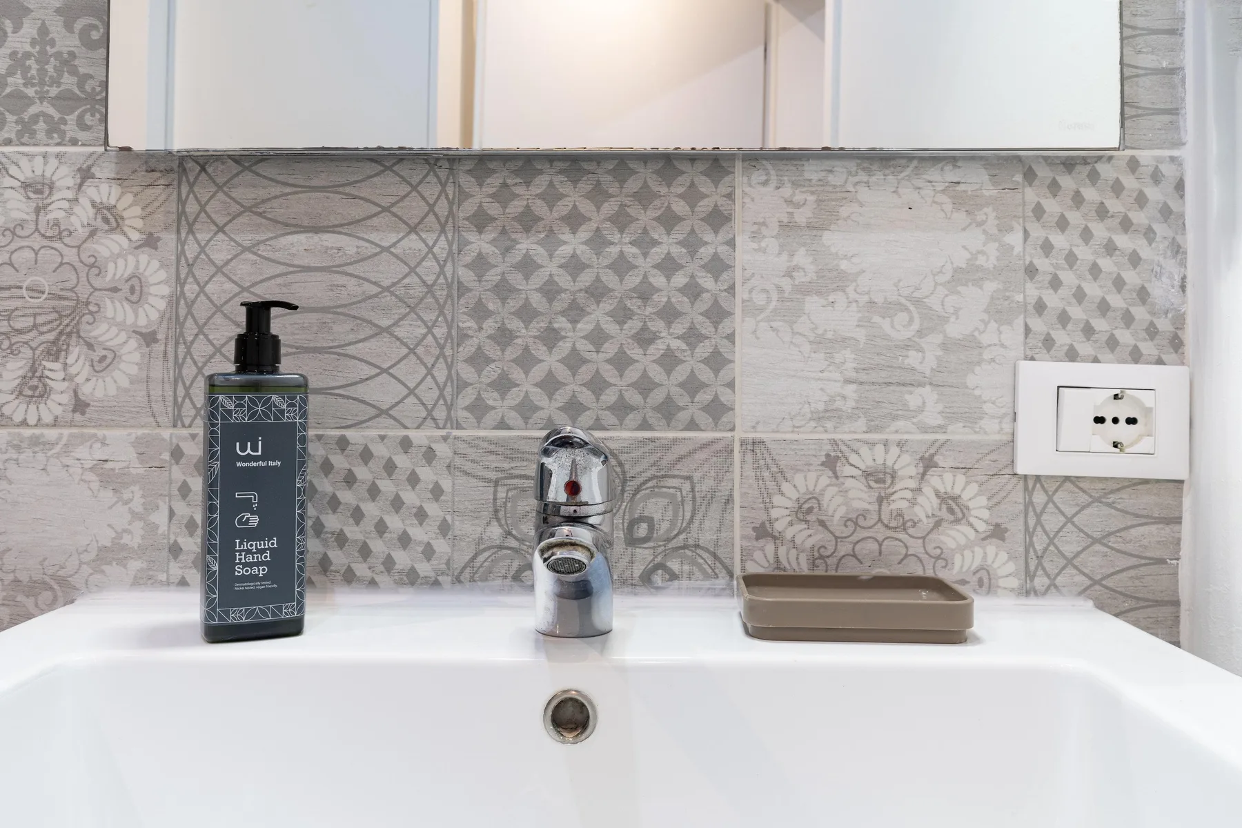 Un lavabo de baño con grifo, dispensador de jabón y azulejos estampados.