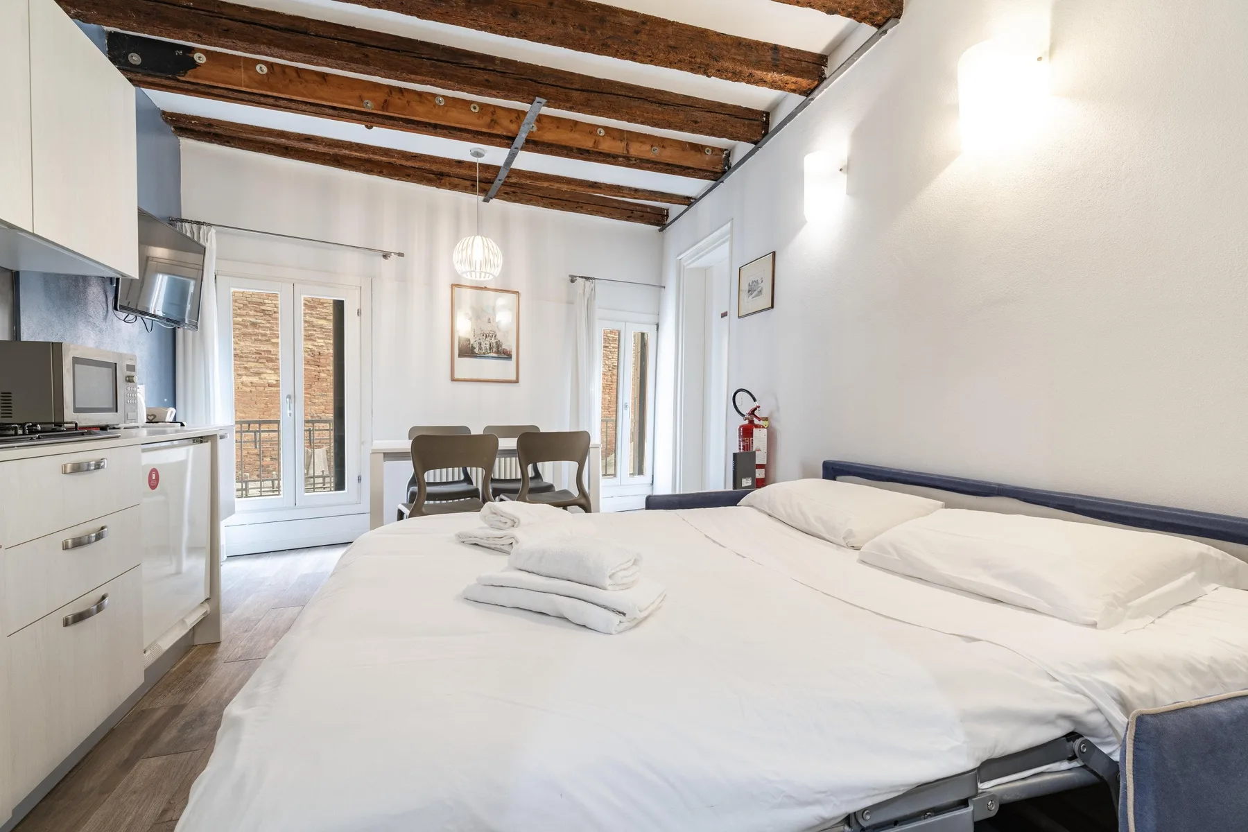 Un dormitorio luminoso con una cama grande y un pequeño comedor junto a las ventanas.