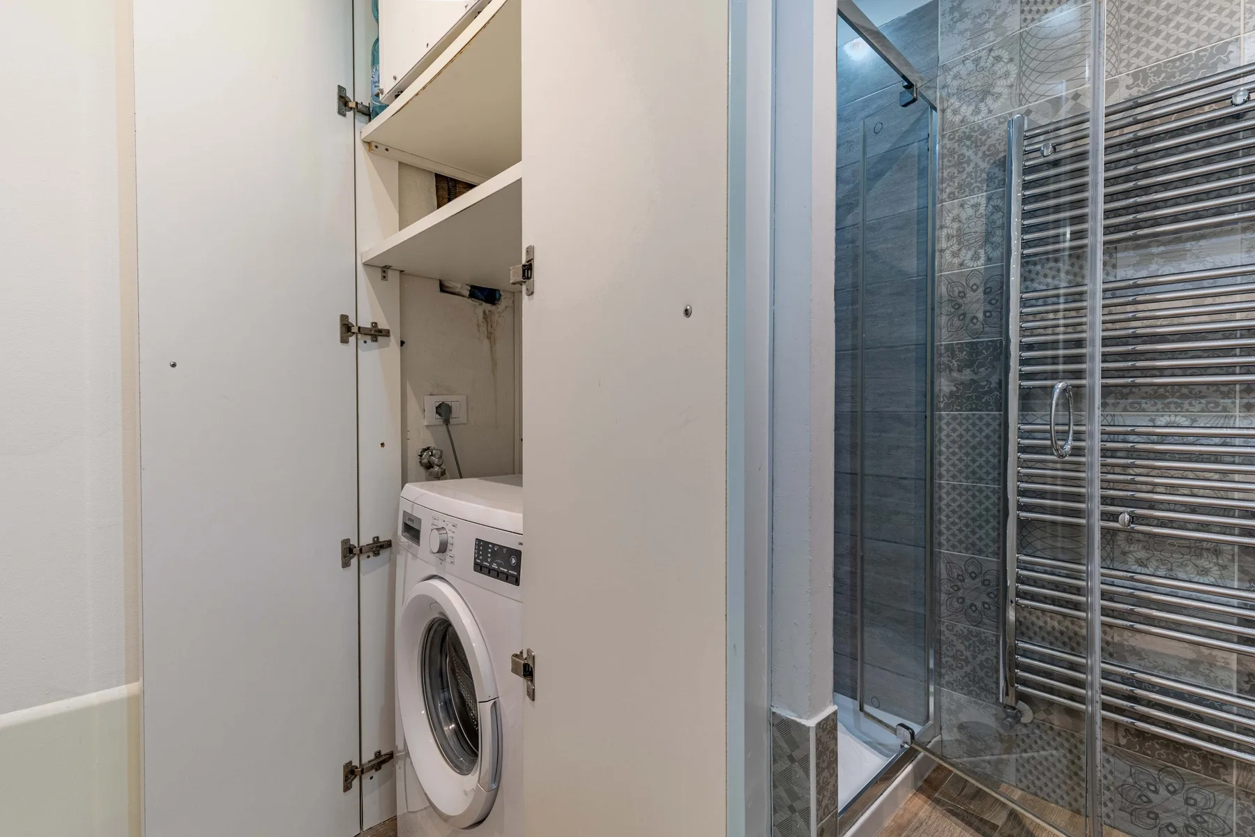 Un baño con una lavadora en un armario junto a una ducha de vidrio.