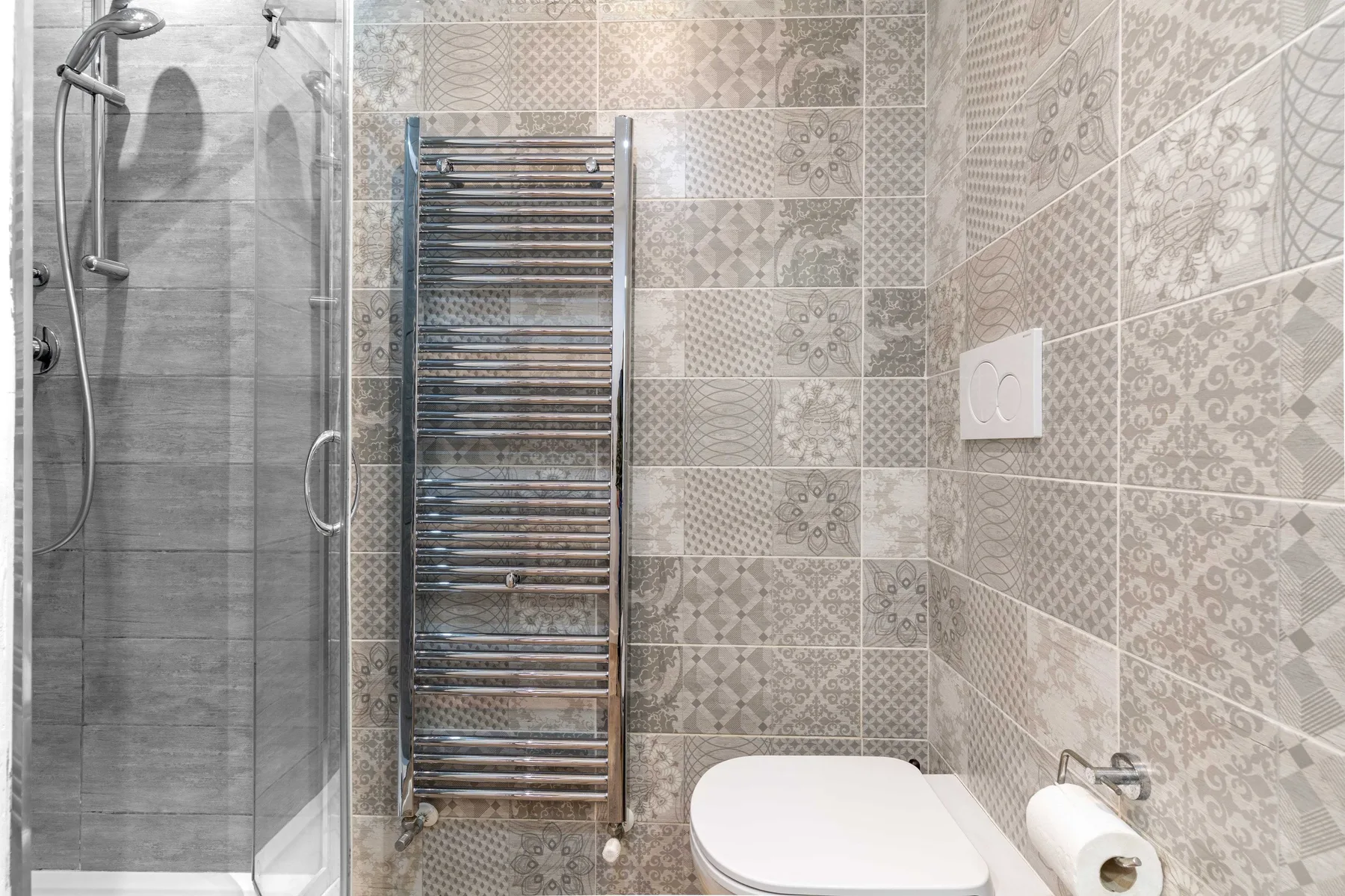 Un baño alicatado con ducha de vidrio, toallero calefactado e inodoro.