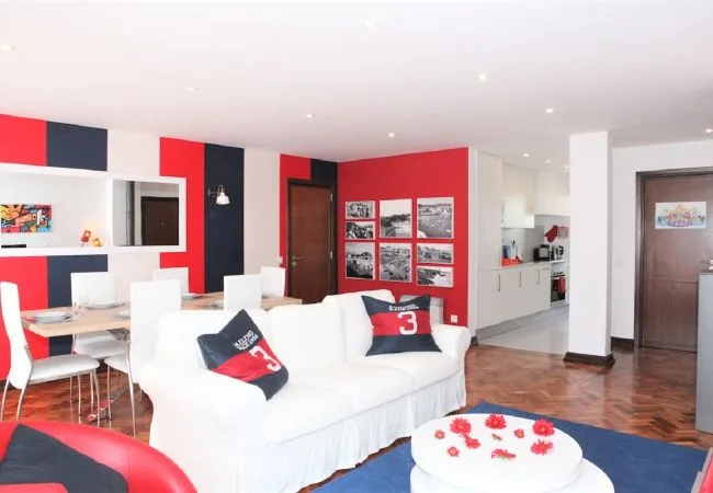 A bright living and dining area features white seating beside a red accent wall.