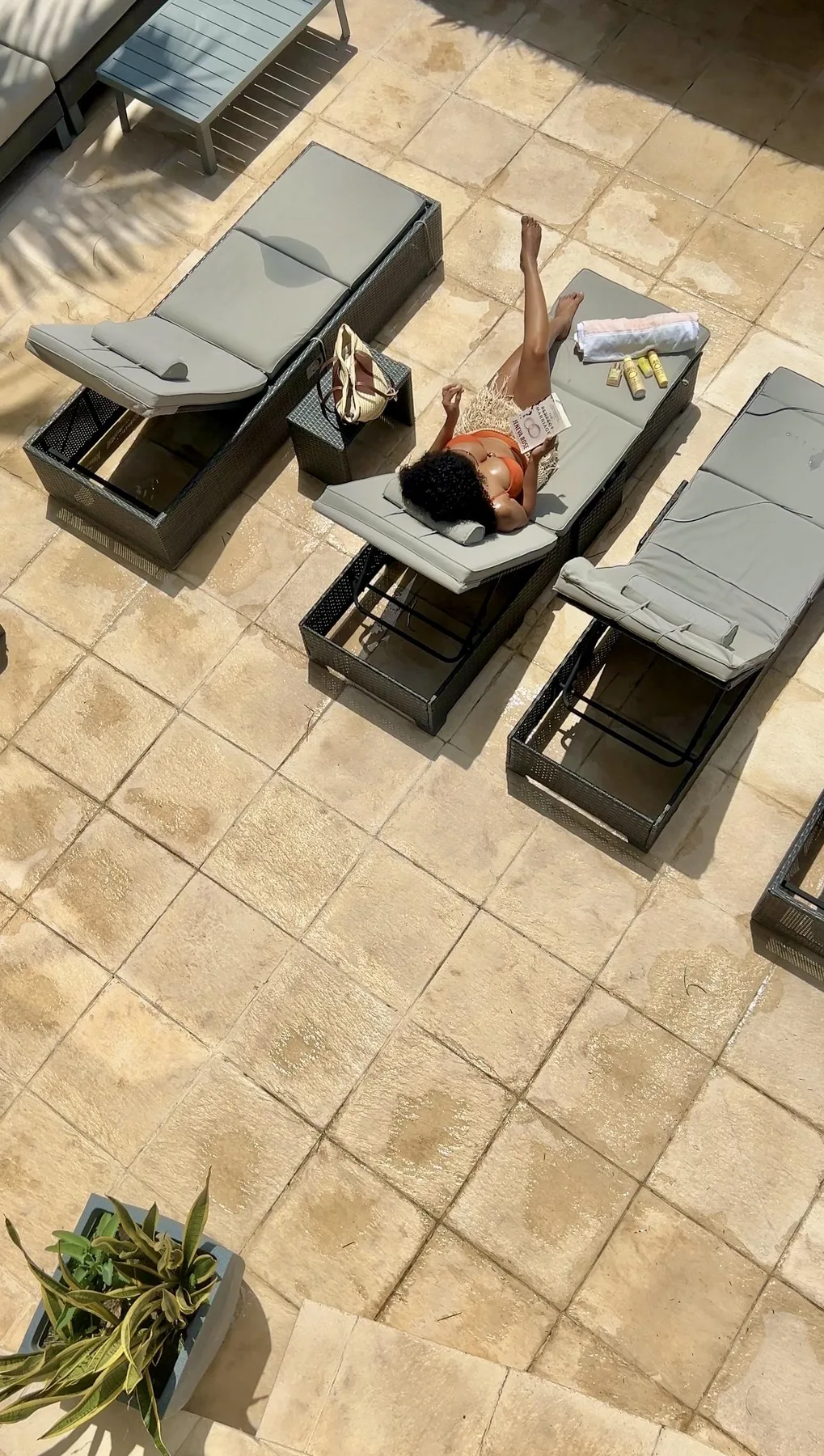 A sunlit tiled patio with lounge seating and a person reclining.