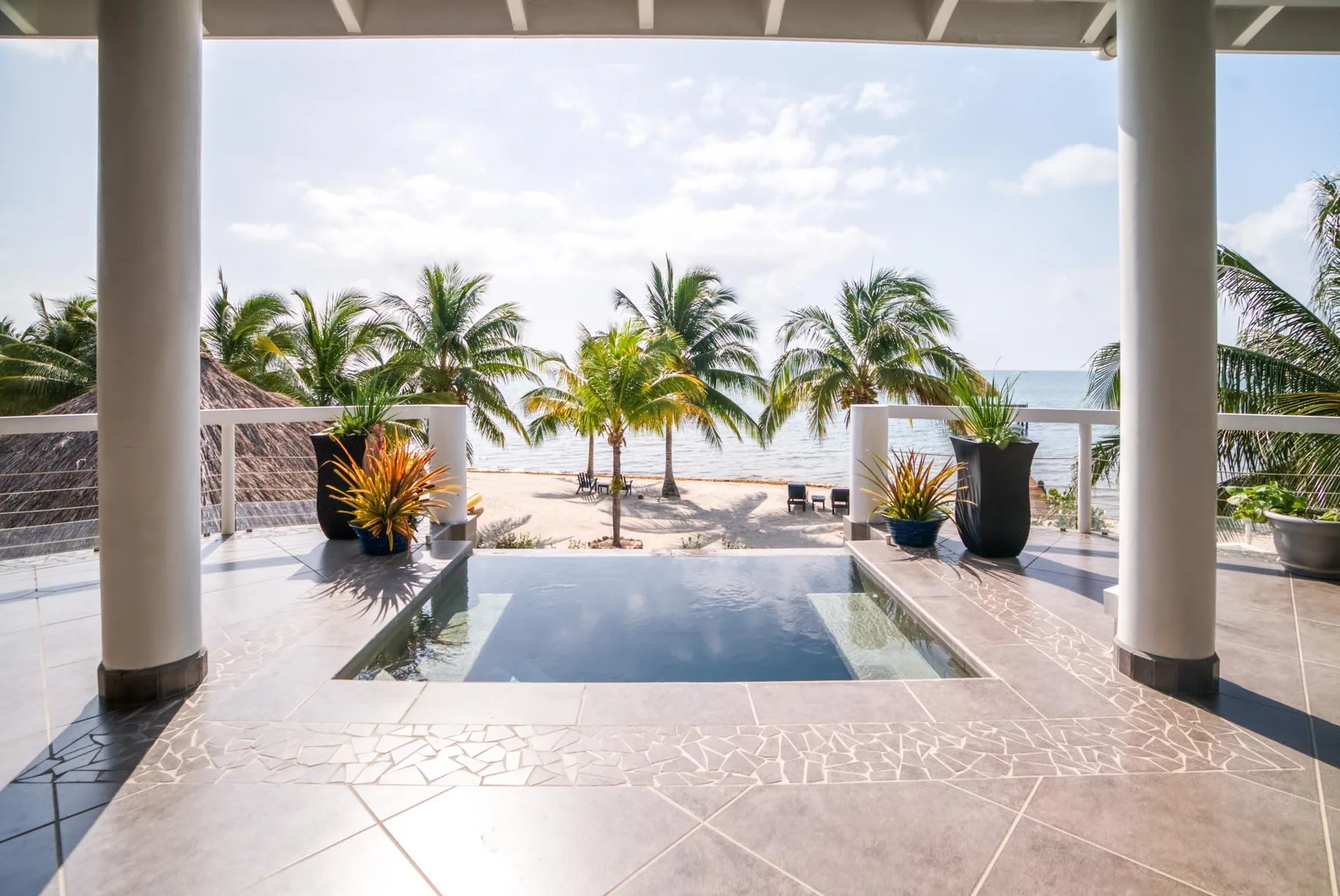 A covered terrace opens onto a small pool, palm trees, and the ocean.