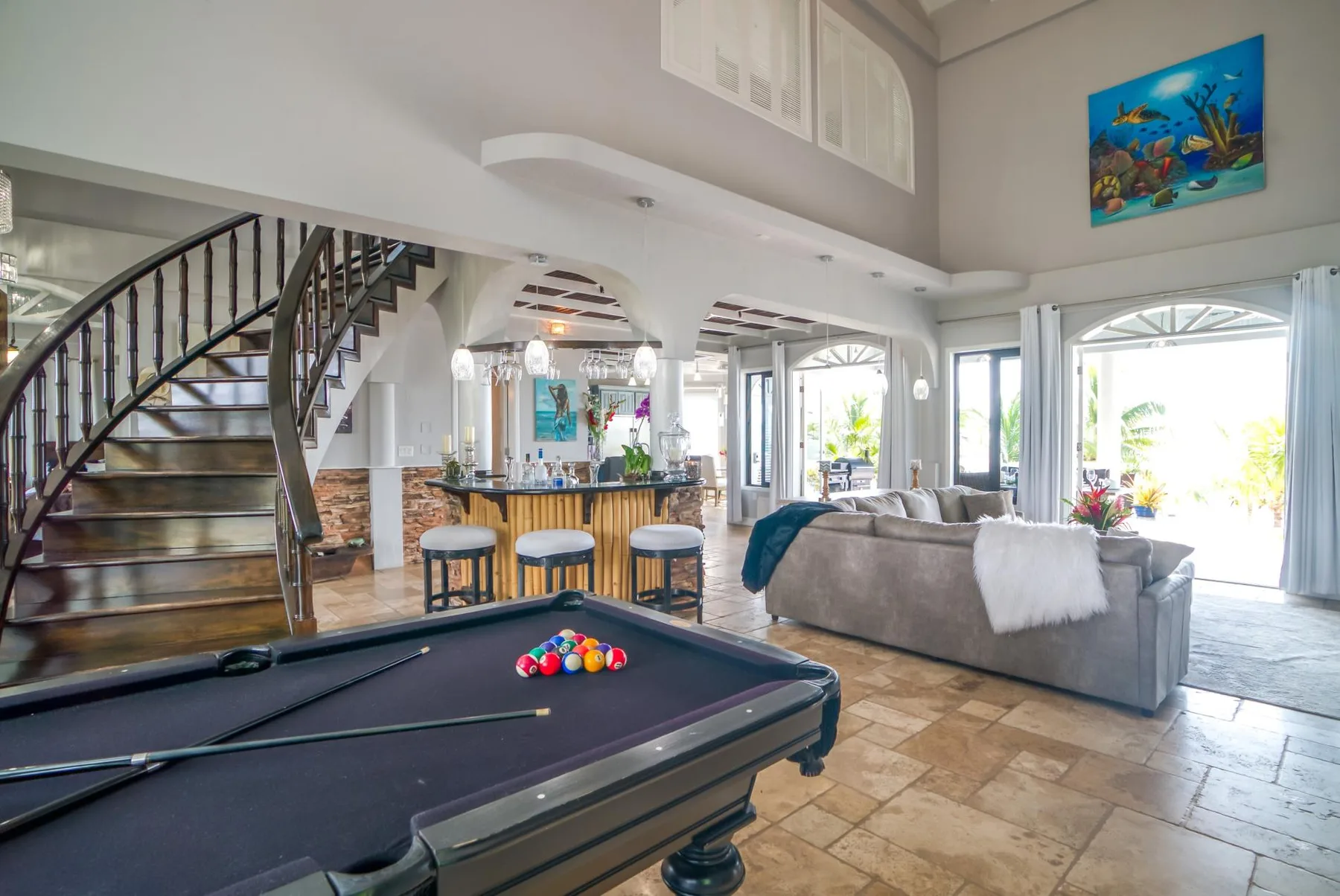 A spacious living room with a pool table, seating, and a kitchen bar.