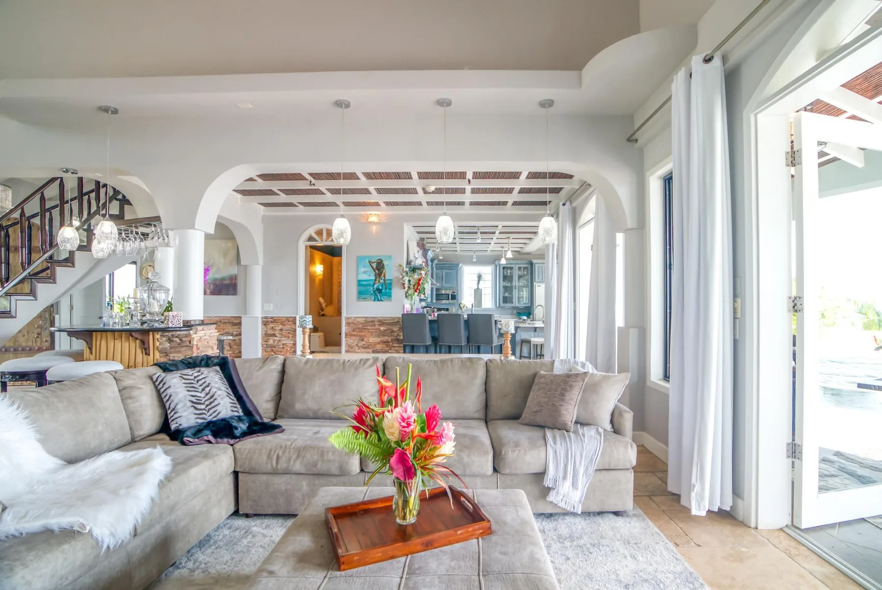 A bright living room features a large sectional seating area and a flower arrangement.