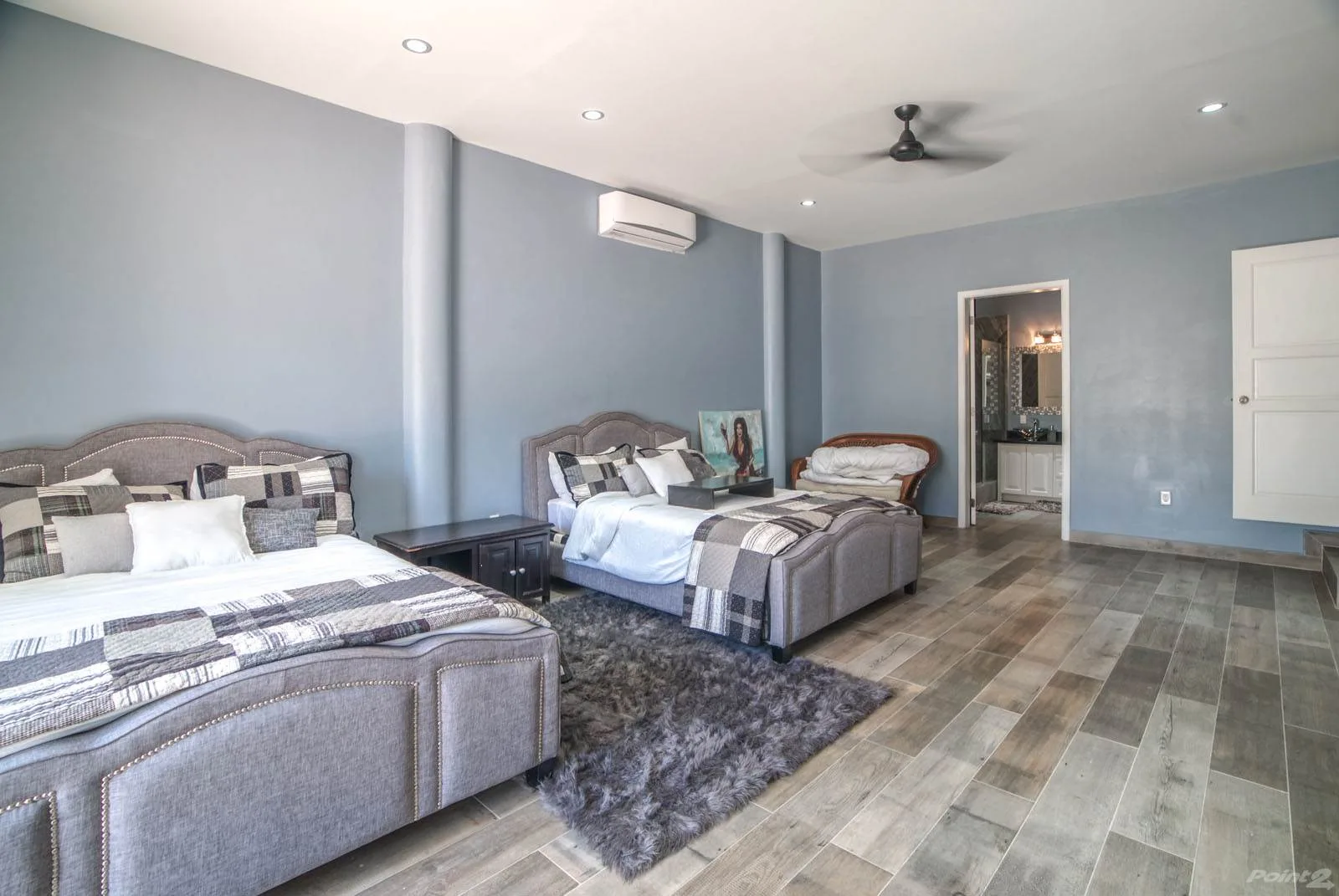 A bedroom with two beds, gray bedding, and a ceiling fan.