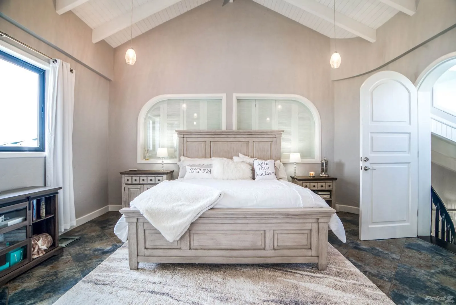 A bright bedroom centers on a large bed beneath a vaulted ceiling.