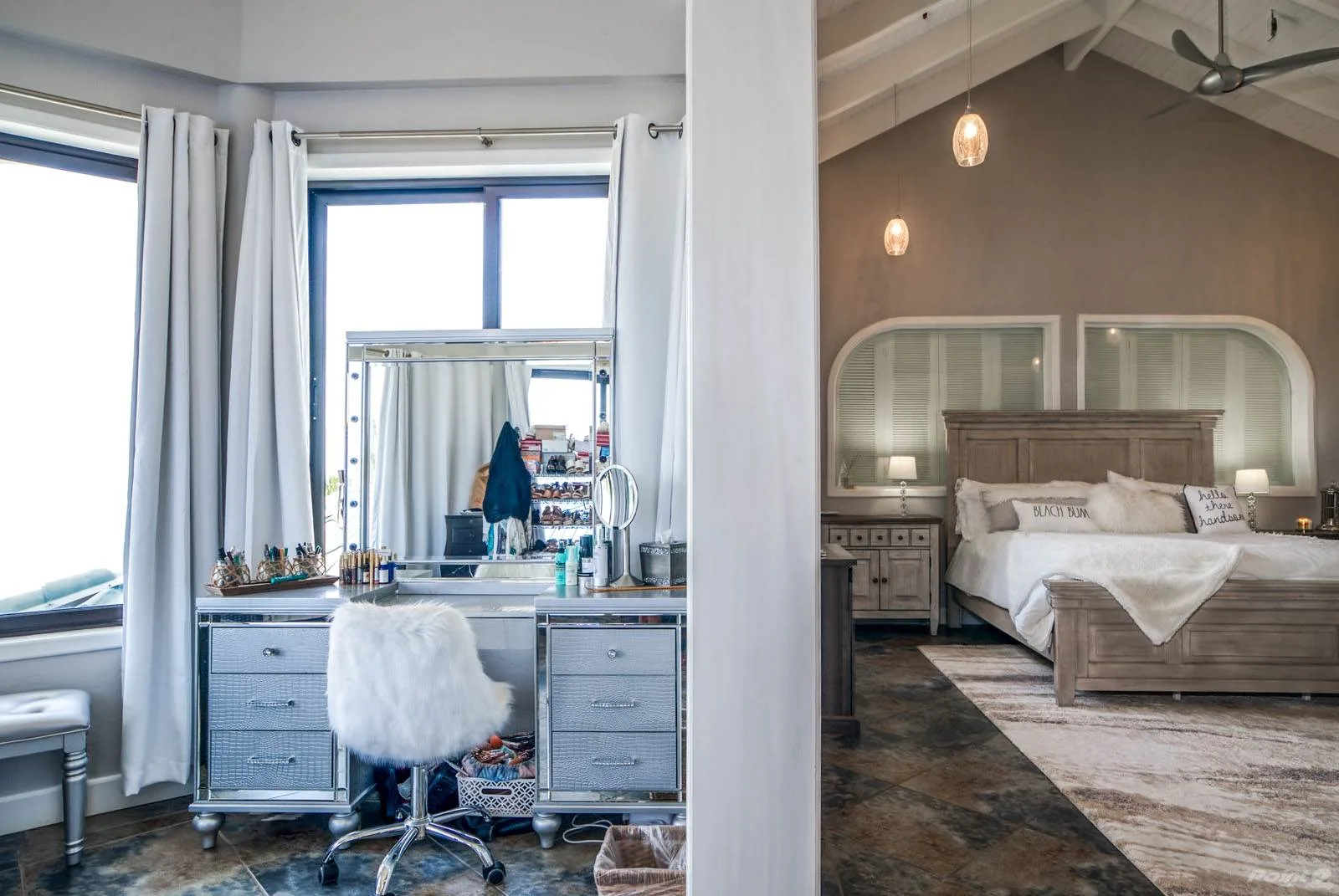 A bedroom with a bed and a vanity beside large windows.