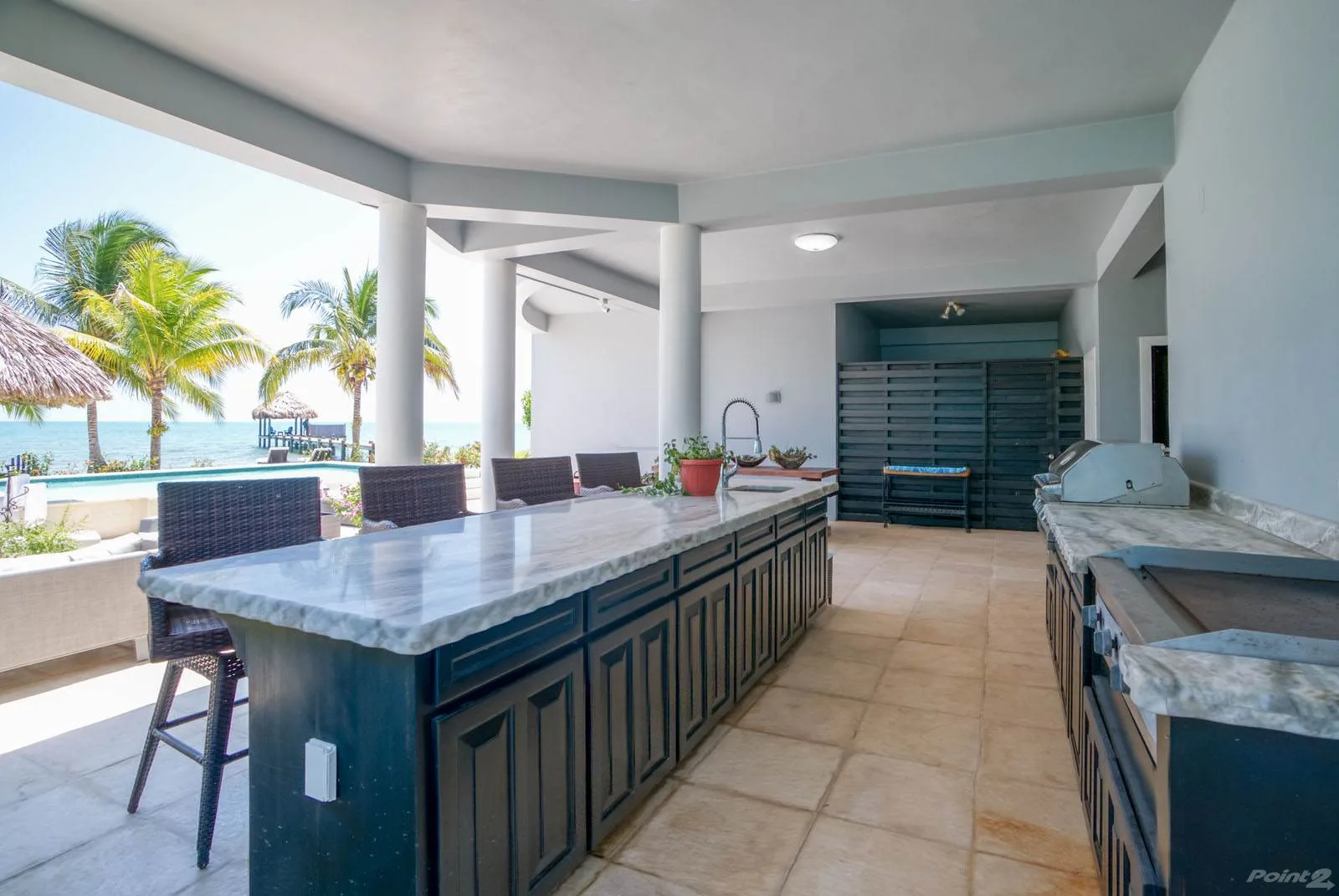 A covered outdoor kitchen with a long counter overlooking palm trees and the water.