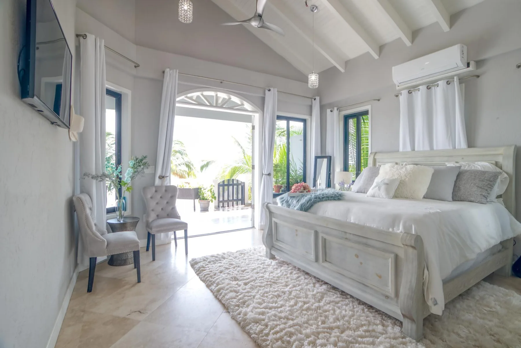 A bright bedroom with a large bed and curtains opening onto a balcony.