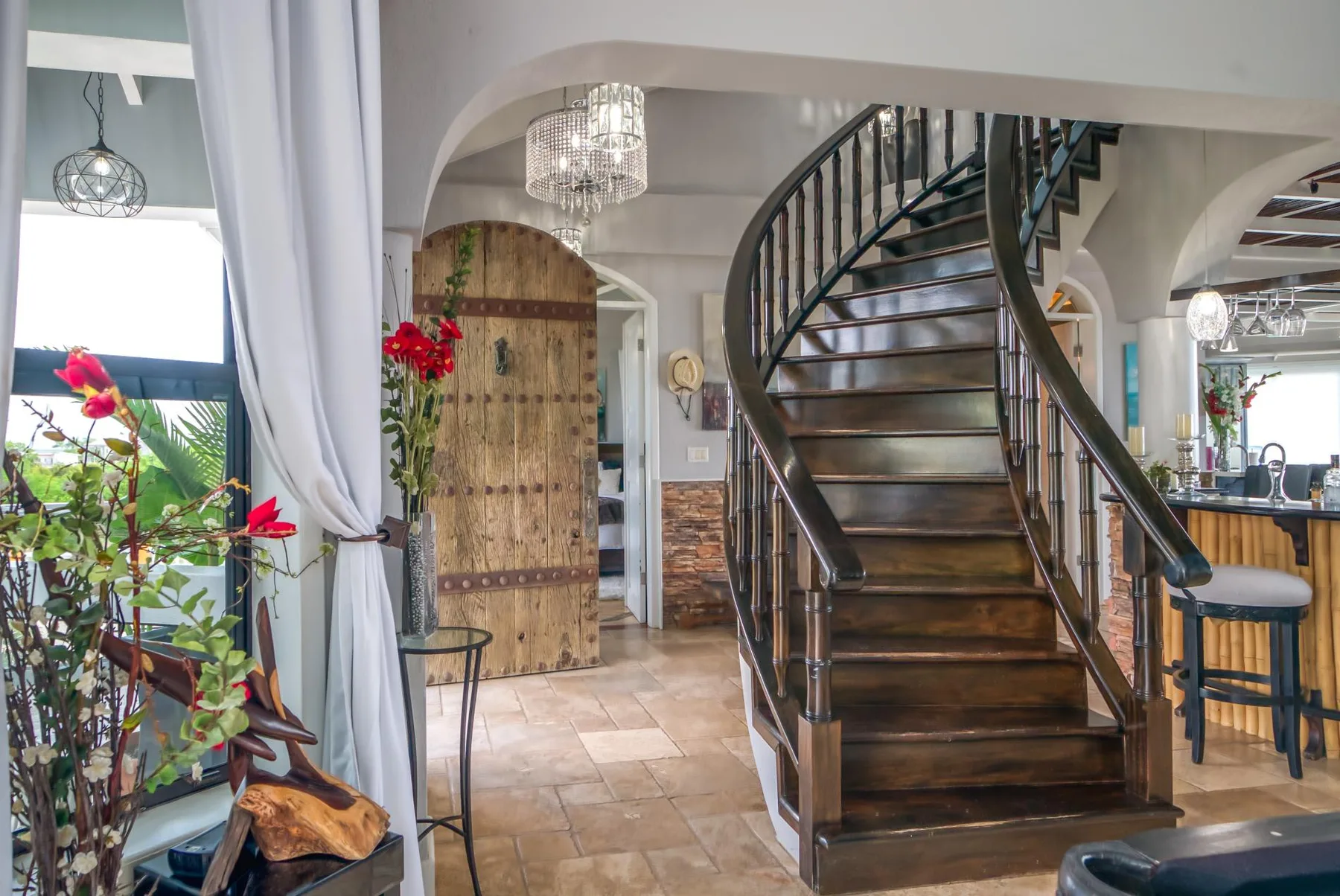 An interior foyer features a curved staircase and a wooden arched door.