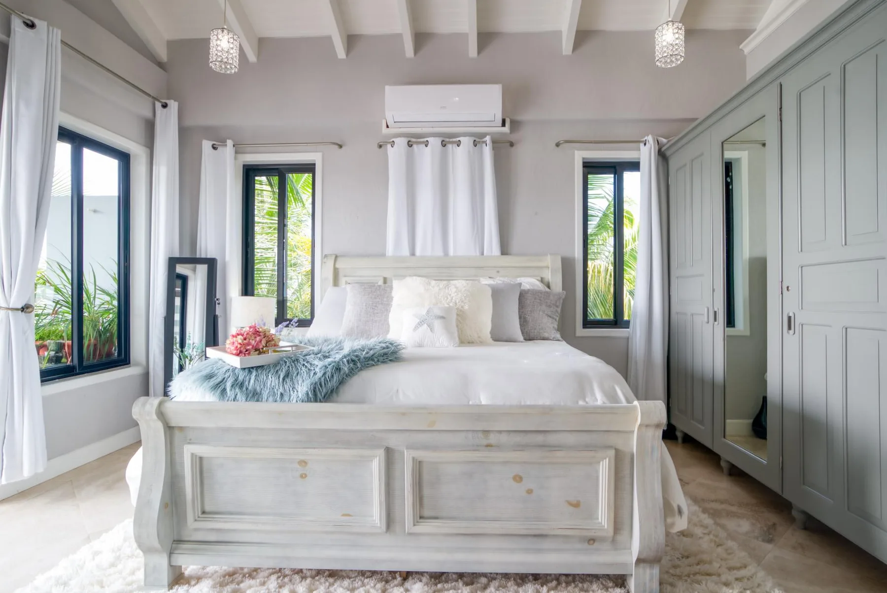 A bright bedroom with a white bed, tall windows, and built-in cabinetry.