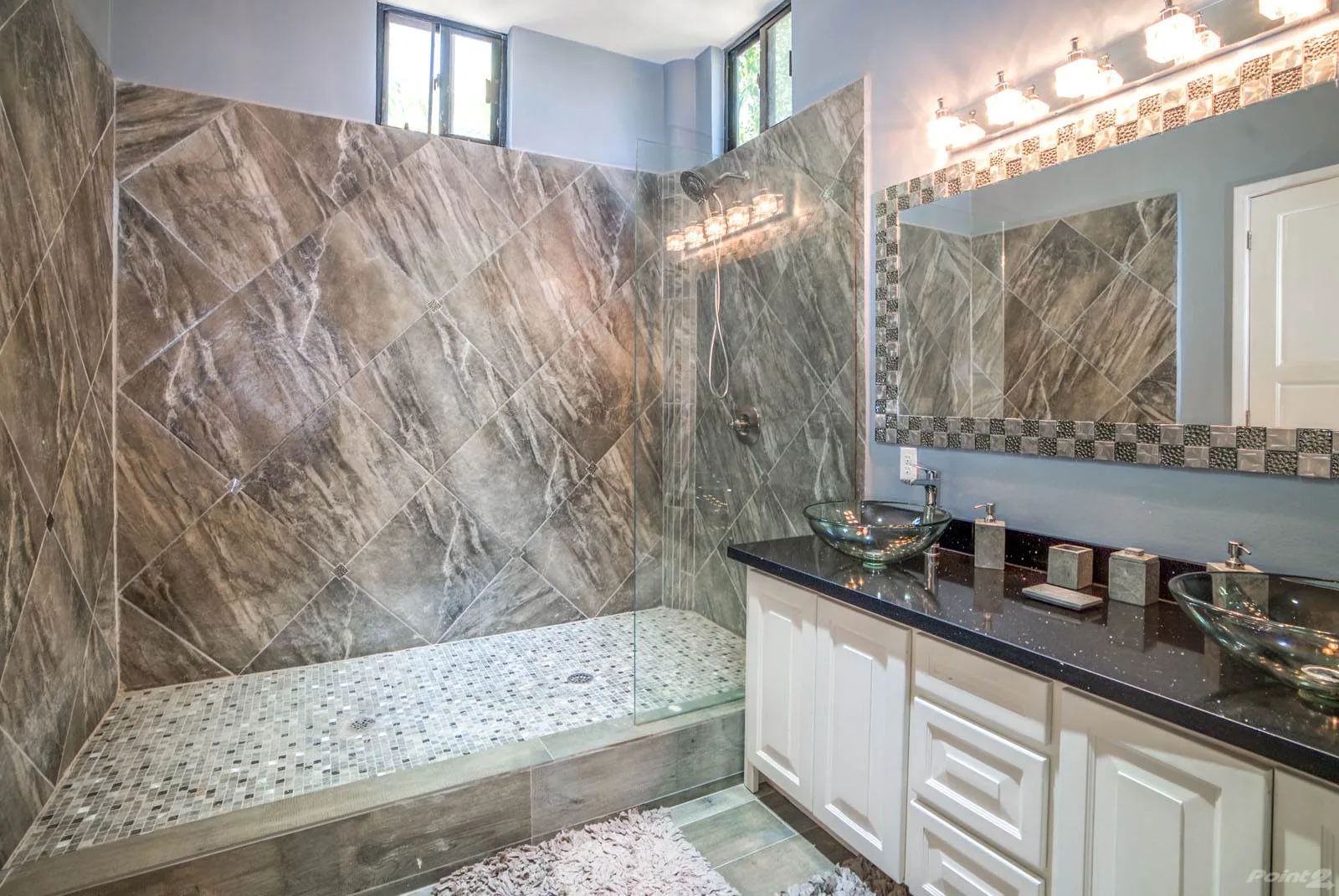 A spacious bathroom has a walk-in shower and a long vanity with a large mirror.