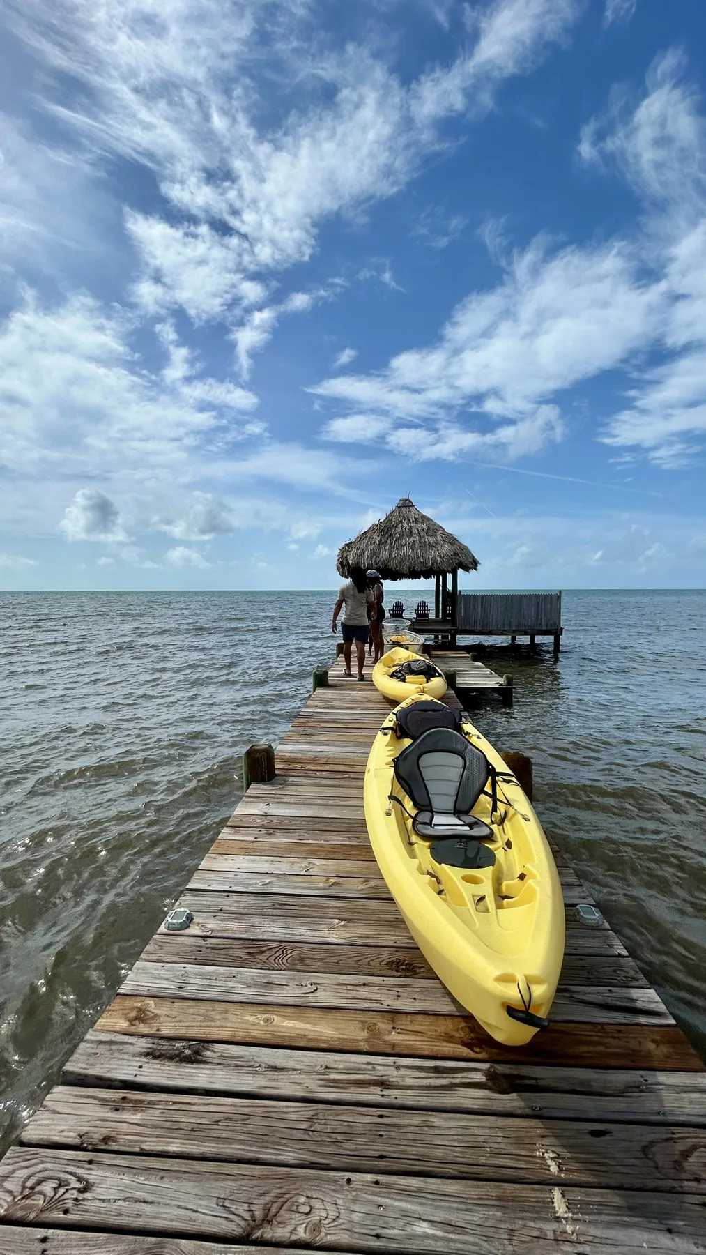 A wooden pier extends over the water, with a yellow kayak beside it.