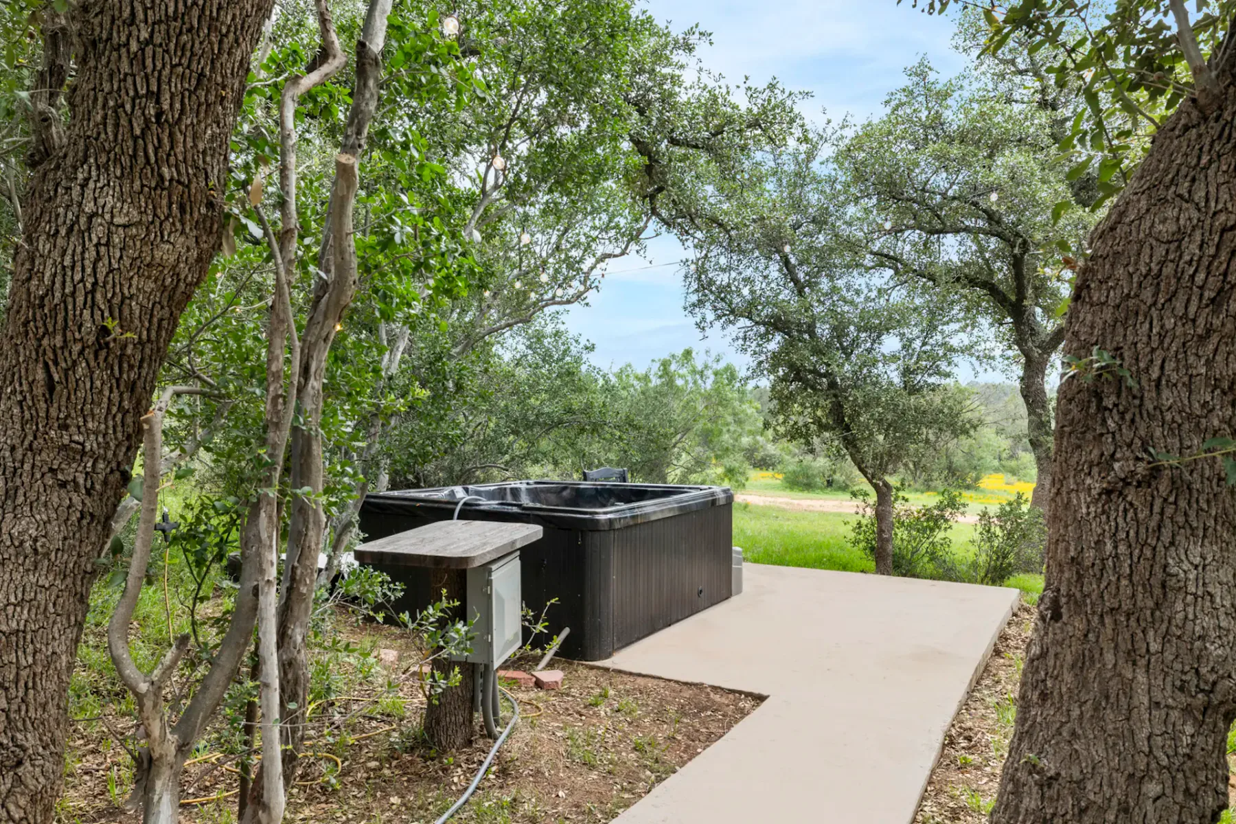 An outdoor hot tub sits beside a paved path among trees.