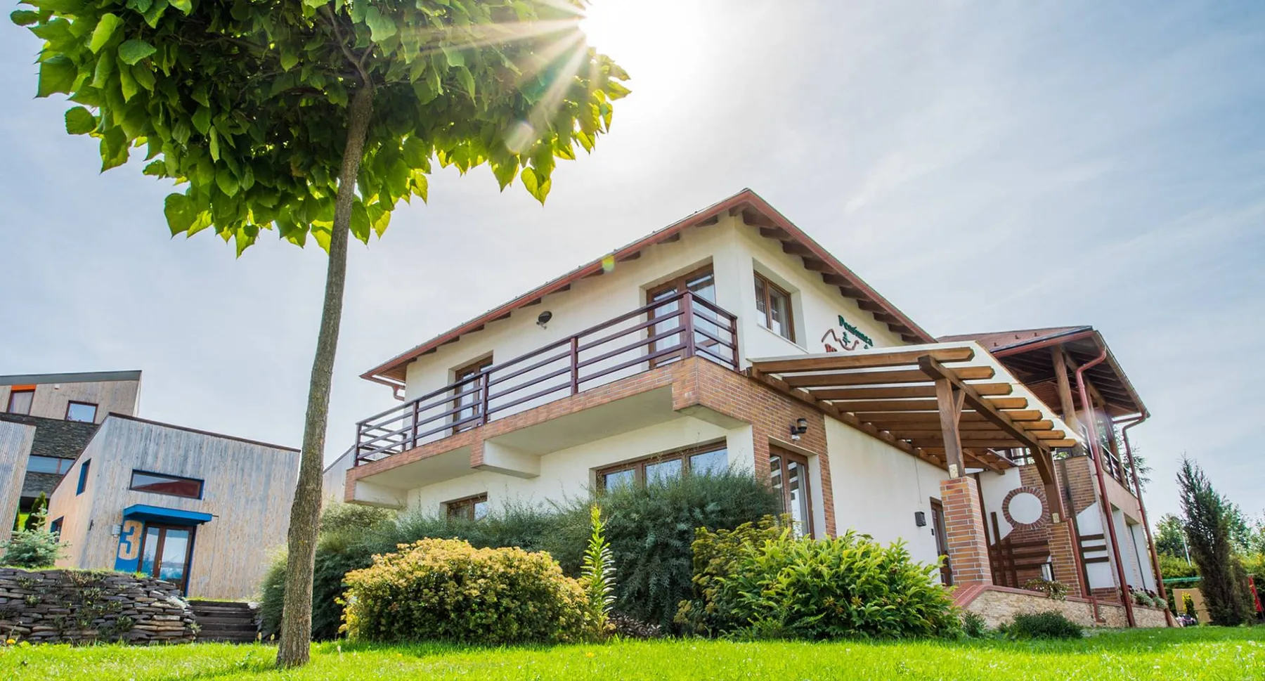 Espacio representativo del hotel: Una casa de dos pisos está junto a un césped y un árbol frondoso.