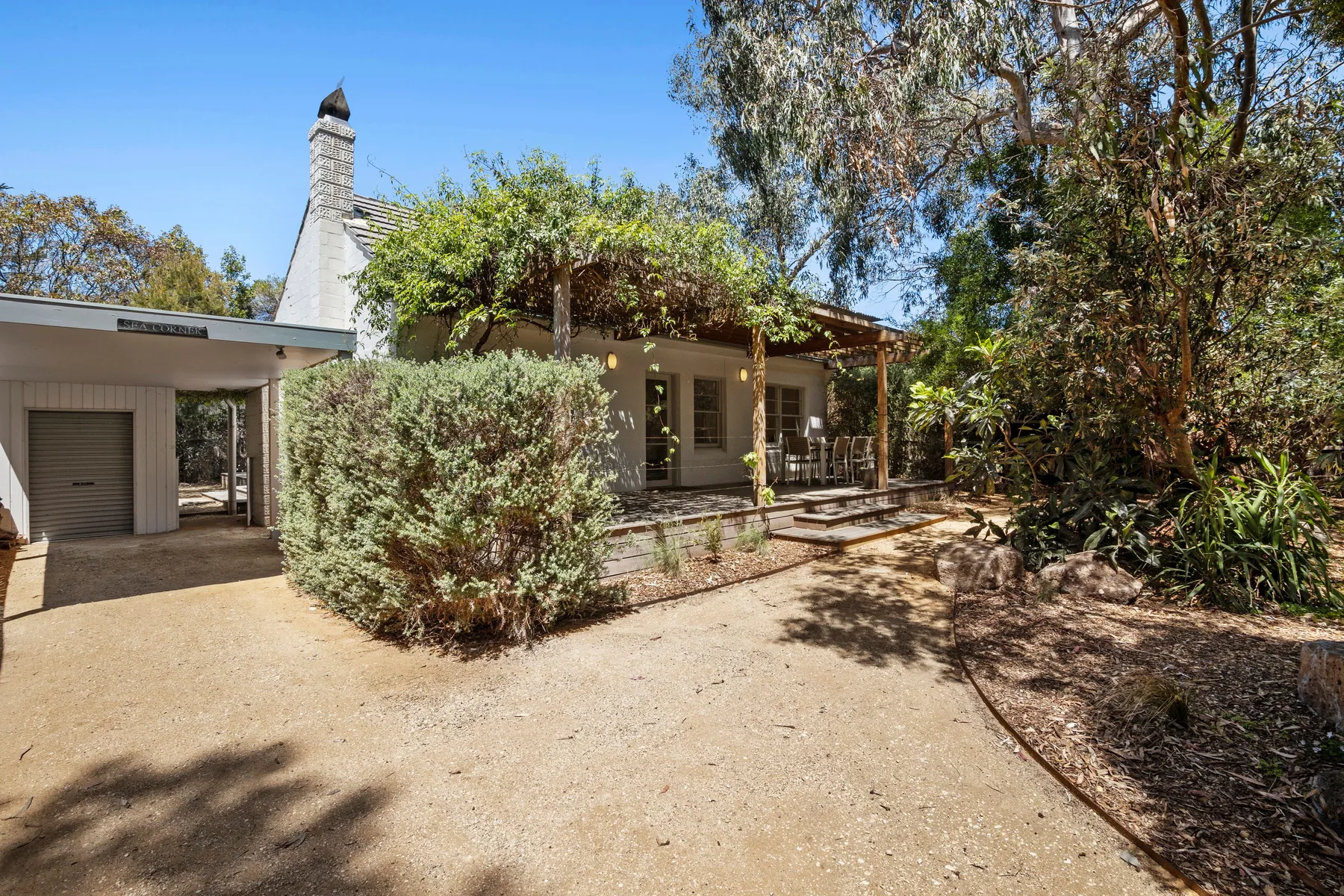 A house with a covered patio opens onto a broad gravel courtyard.