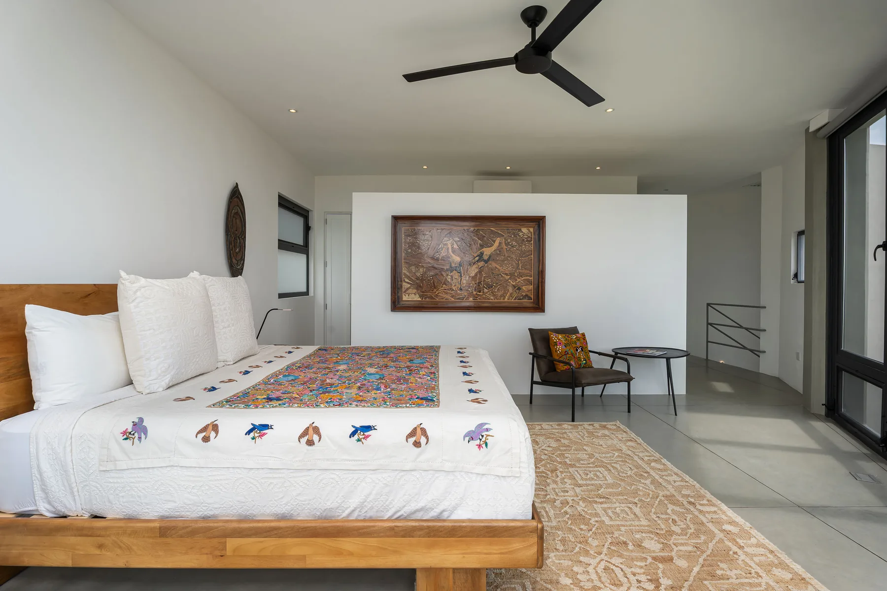 A bedroom with a bed, colorful patterned cover, and wall art.