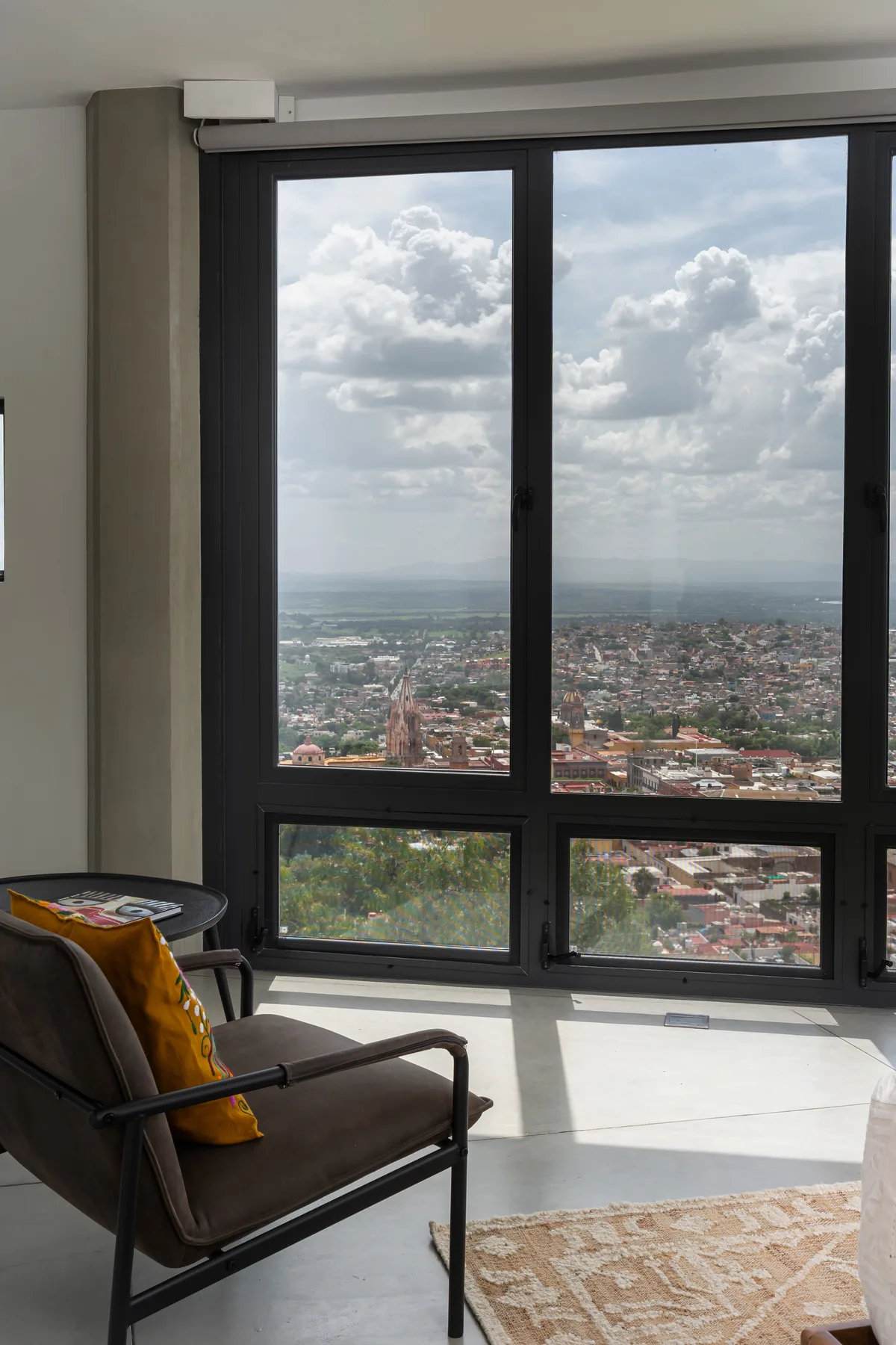 A bright room with a large window overlooking a city and a chair beside it.