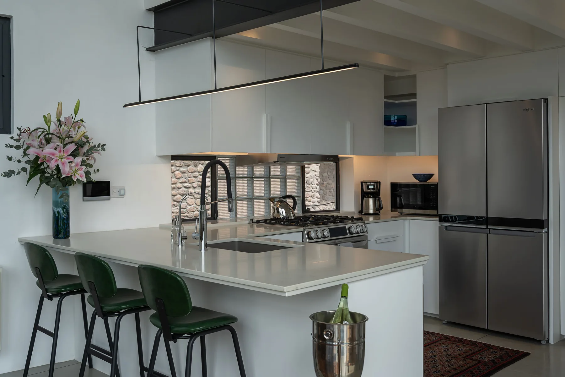 A modern kitchen with a broad island and dark green bar seating.