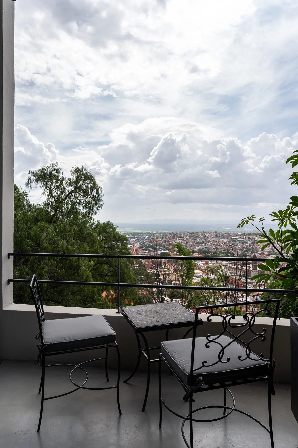A balcony with seating overlooks a city beneath a cloudy sky.