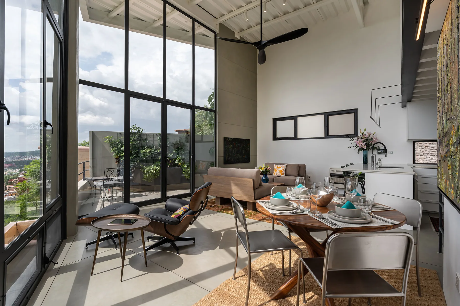 A bright open-plan living and dining area with large windows and a set table.