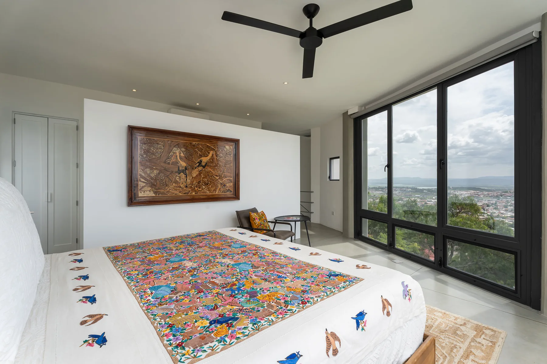 A bedroom with a colorful patterned bedspread and large windows overlooking a landscape.